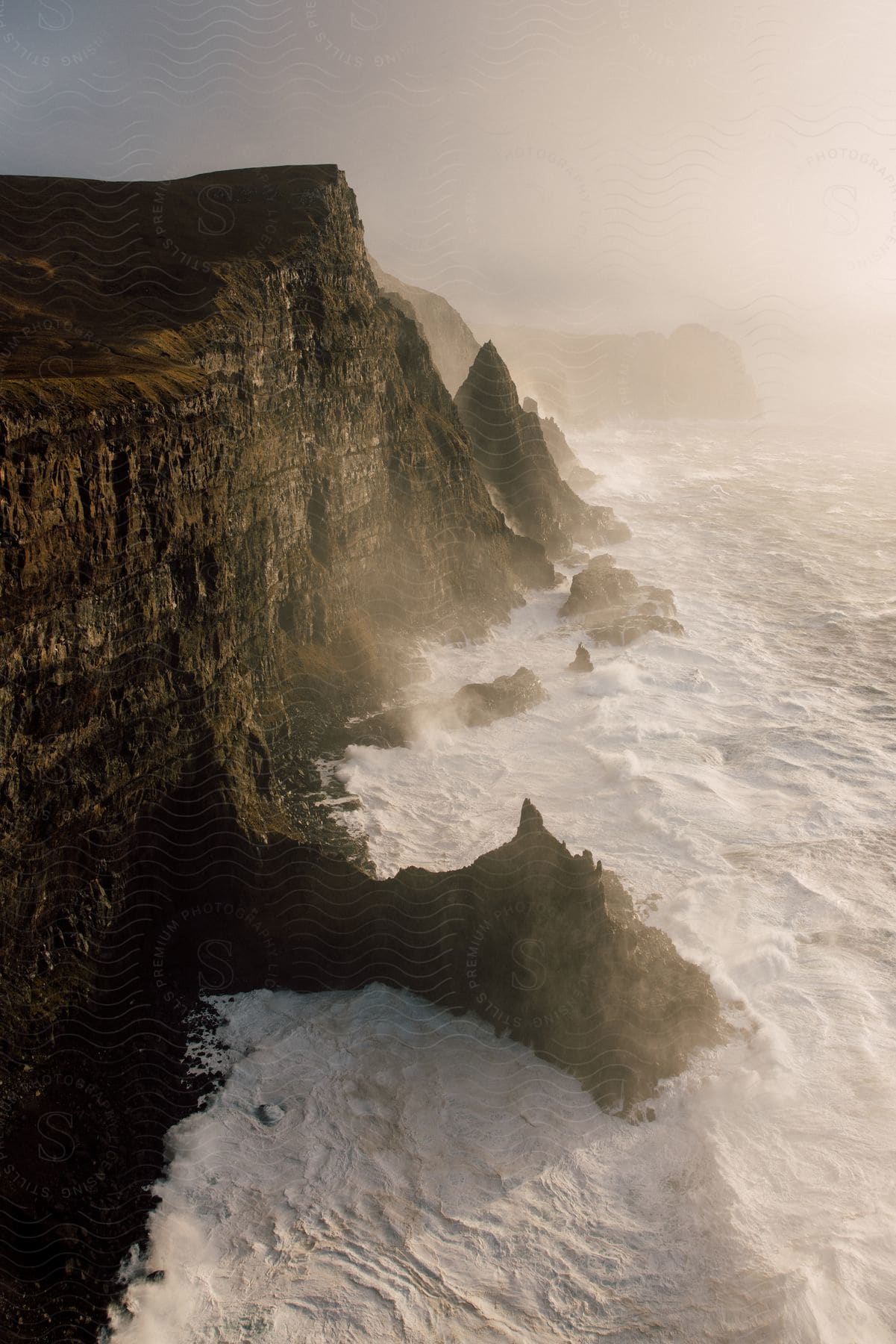 Sunlit waves crash into a mountain cliff along the coast