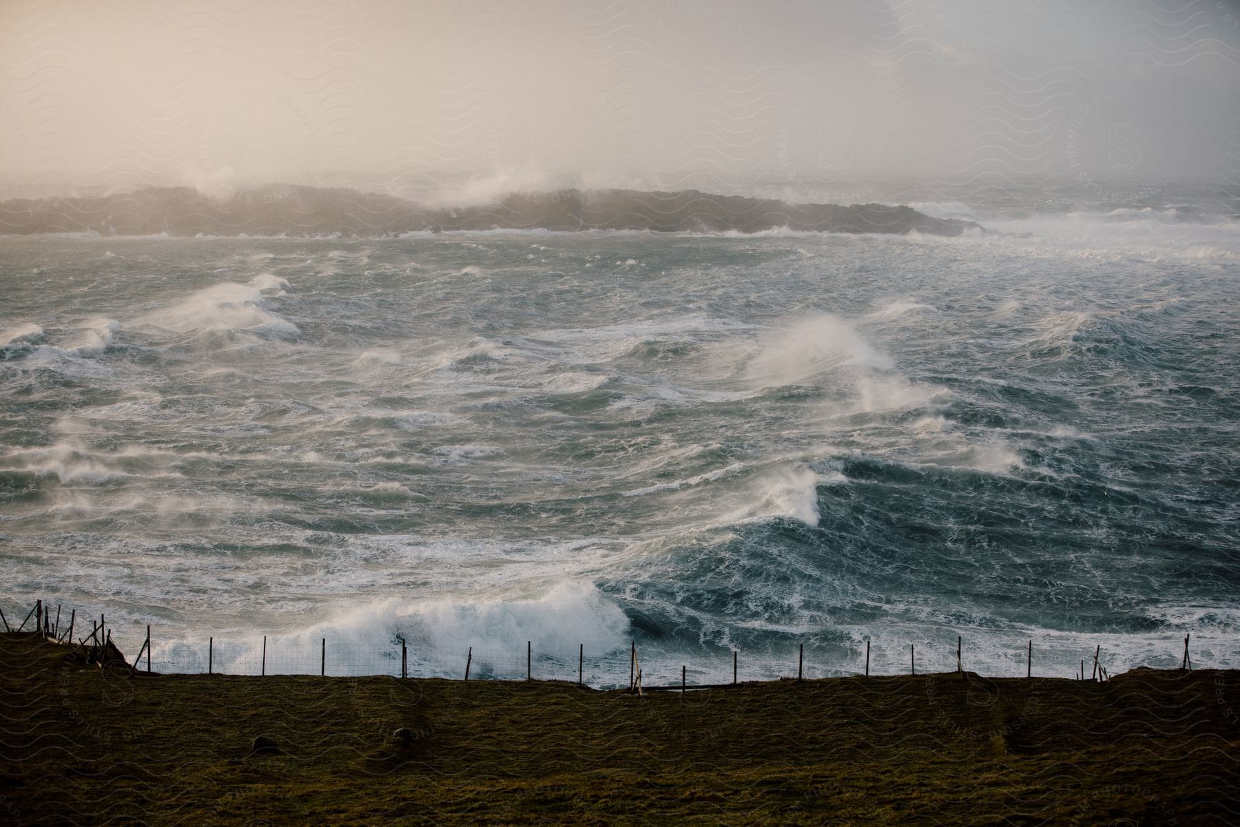 A coastal island with rough seas and furious waves in the background