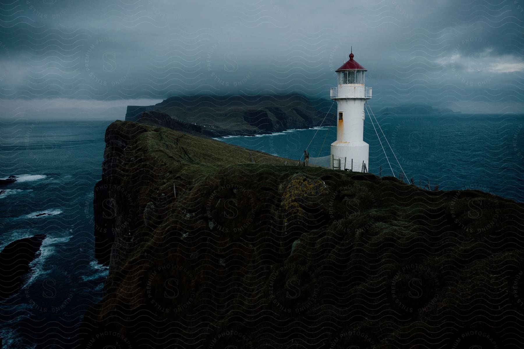 A lighthouse on a cliff overlooking the water under a cloudy sky