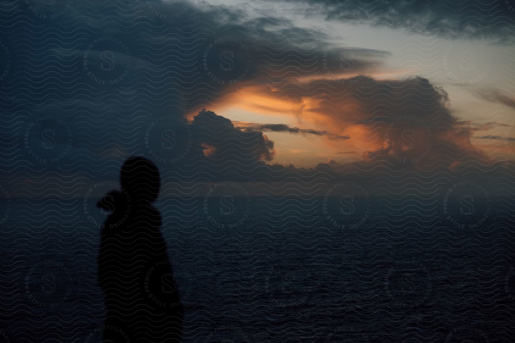 A person wearing a hoodie jacket stands up in front of the vast ocean in the dark