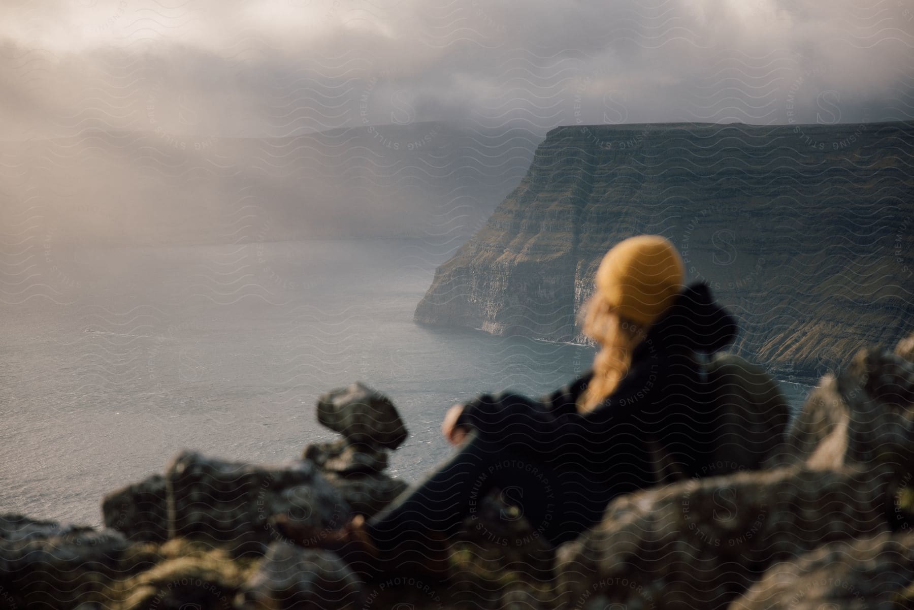 A female hiker resting on rocks looking at foggy coastal cliffs at sunrise