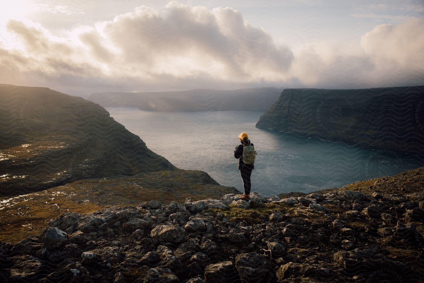 Woman standing on top of a rocky mountain photographing the open sea