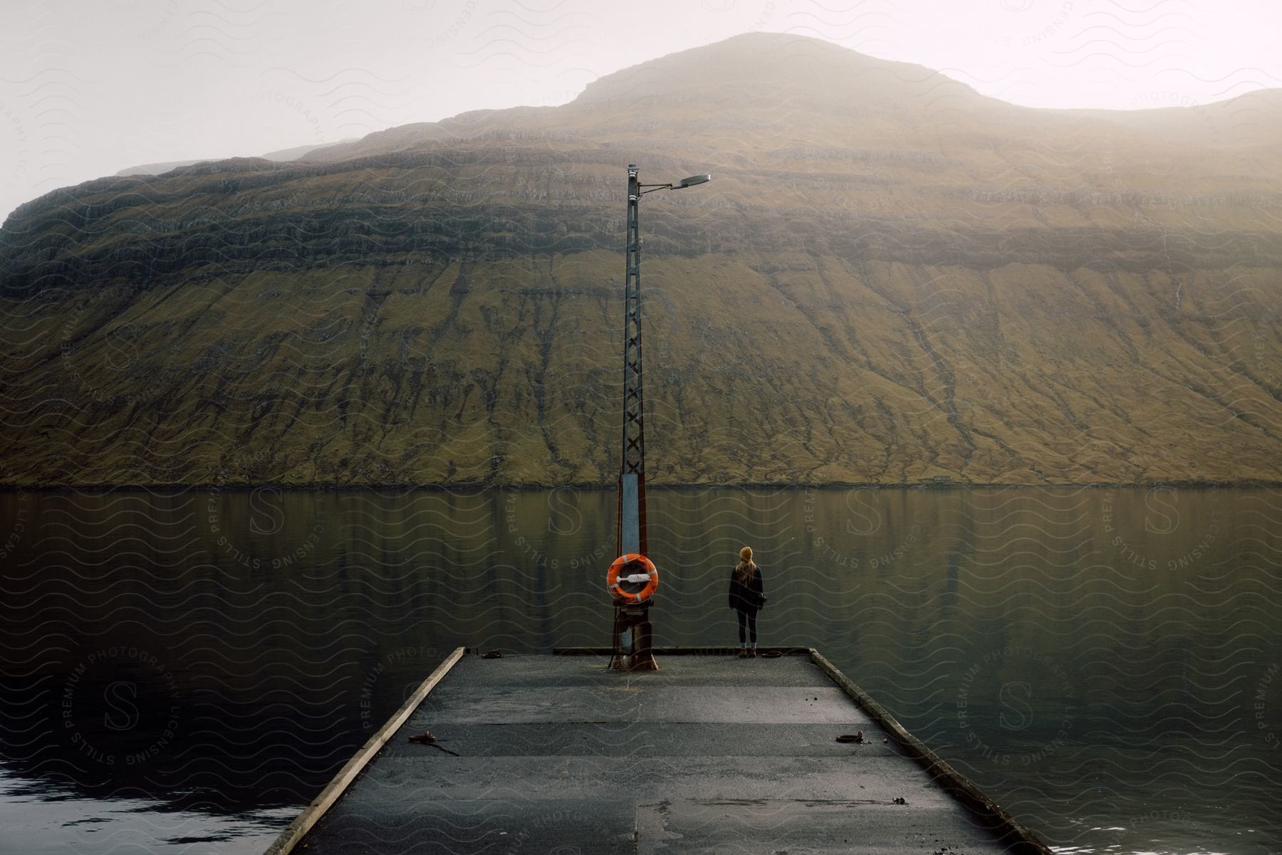 Woman standing on a pier next to a river near a mountain