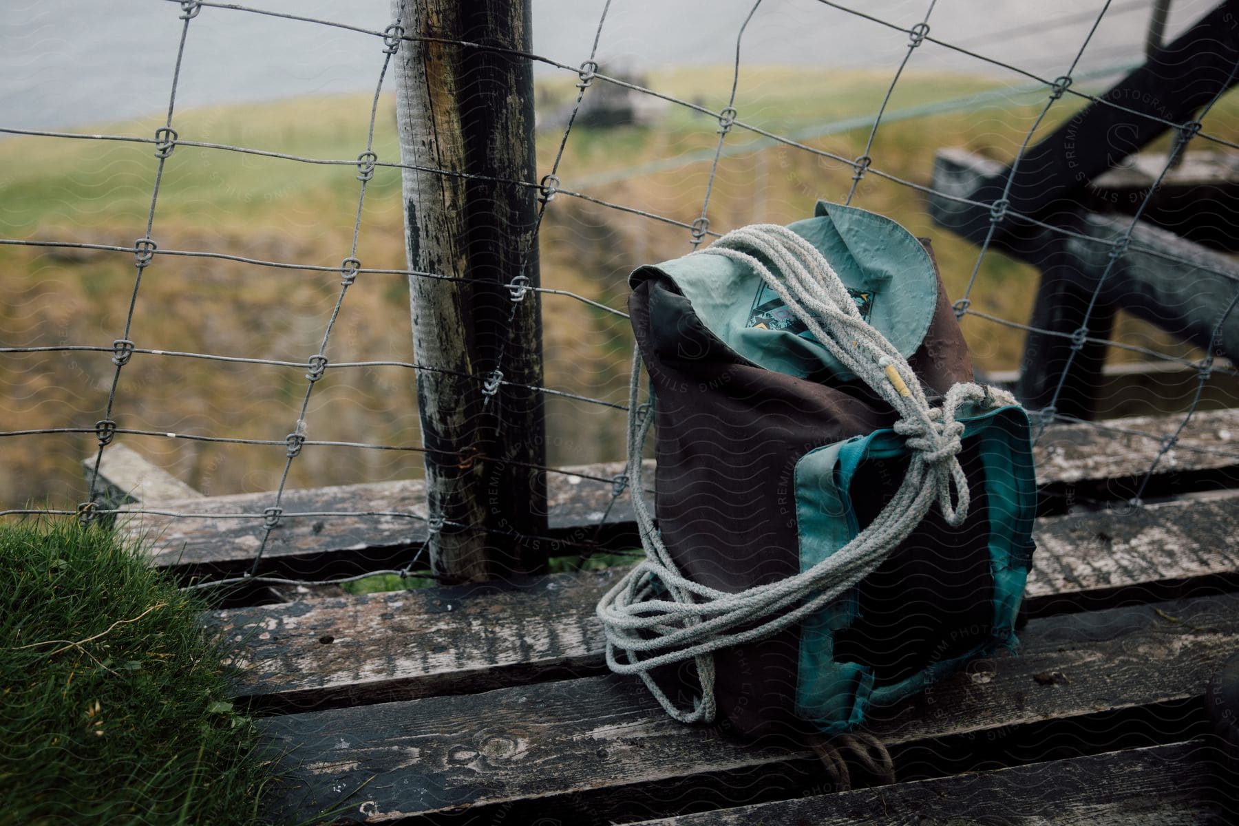 A backpack and length of rope sit near a fence on wooden boards