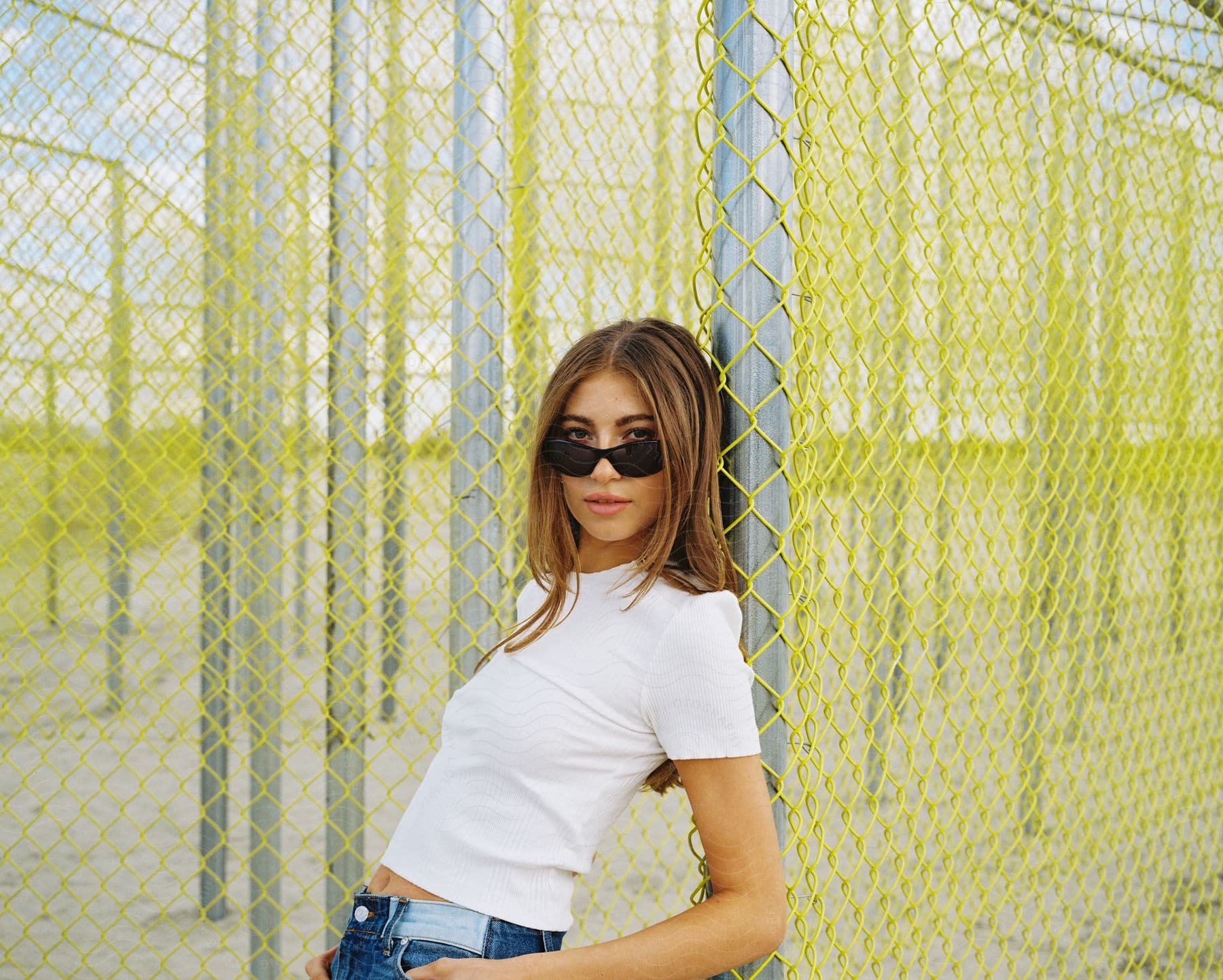 A smiling woman wearing sunglasses stands near a fence