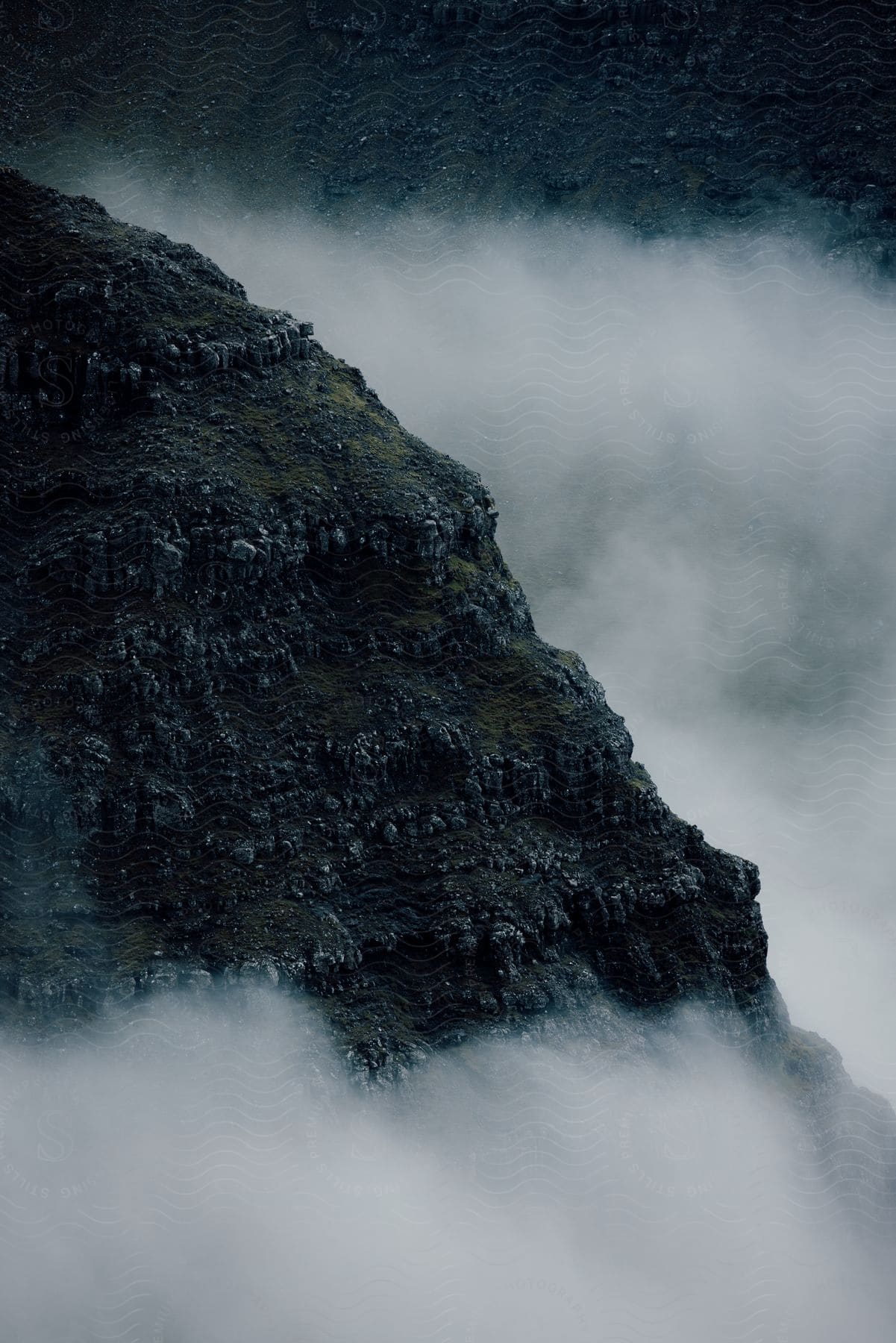 A misty mountain face surrounded by clouds