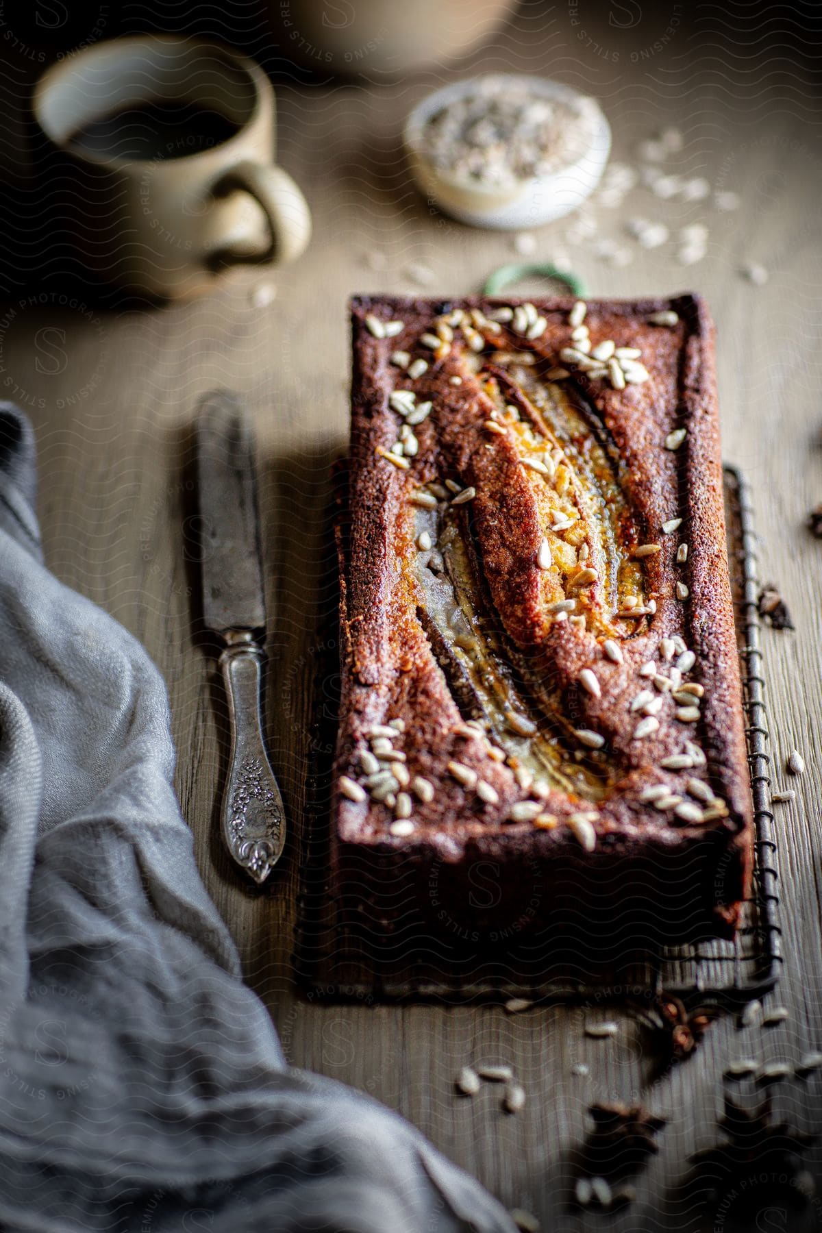 Fresh bread loaf with sesame seeds on wooden table accompanied by a silver knife and a cup of coffee