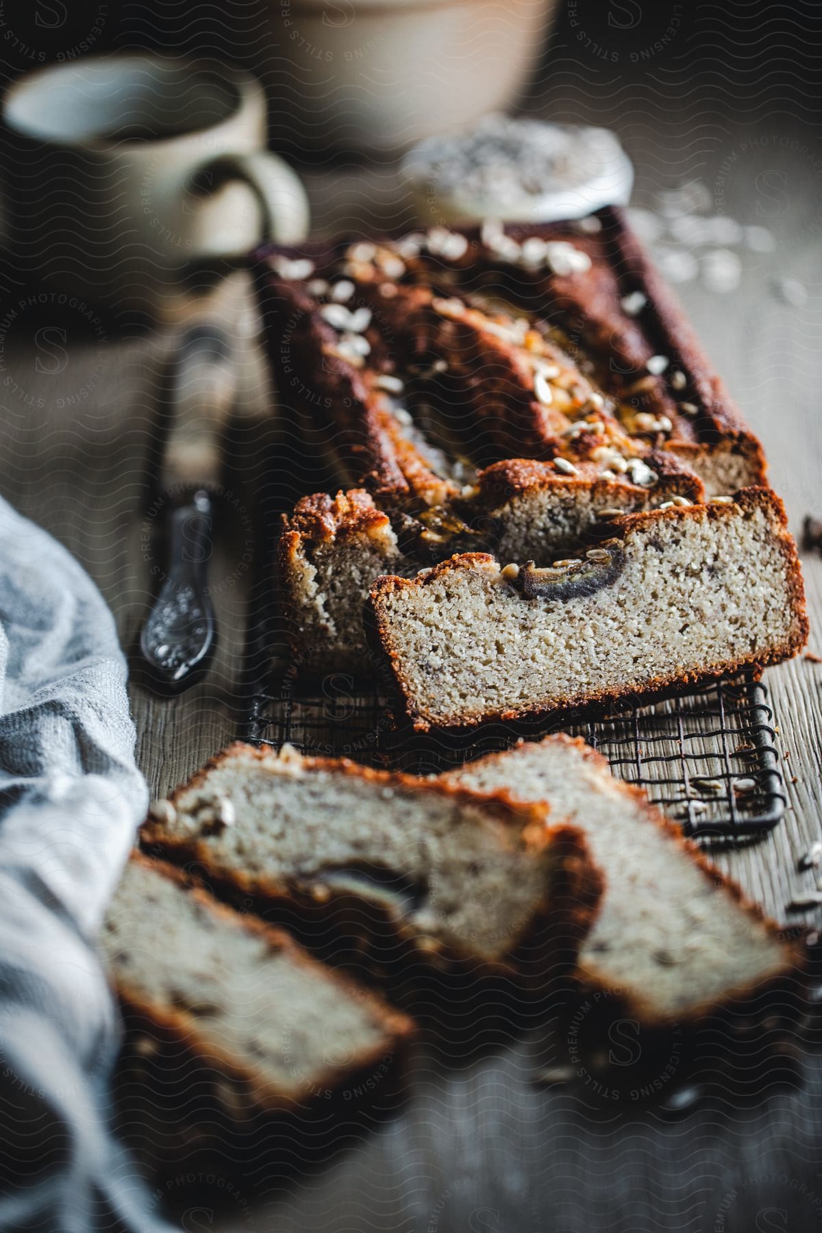 A sliced loaf of banana bread is placed on a wooden table with a knife and cup nearby