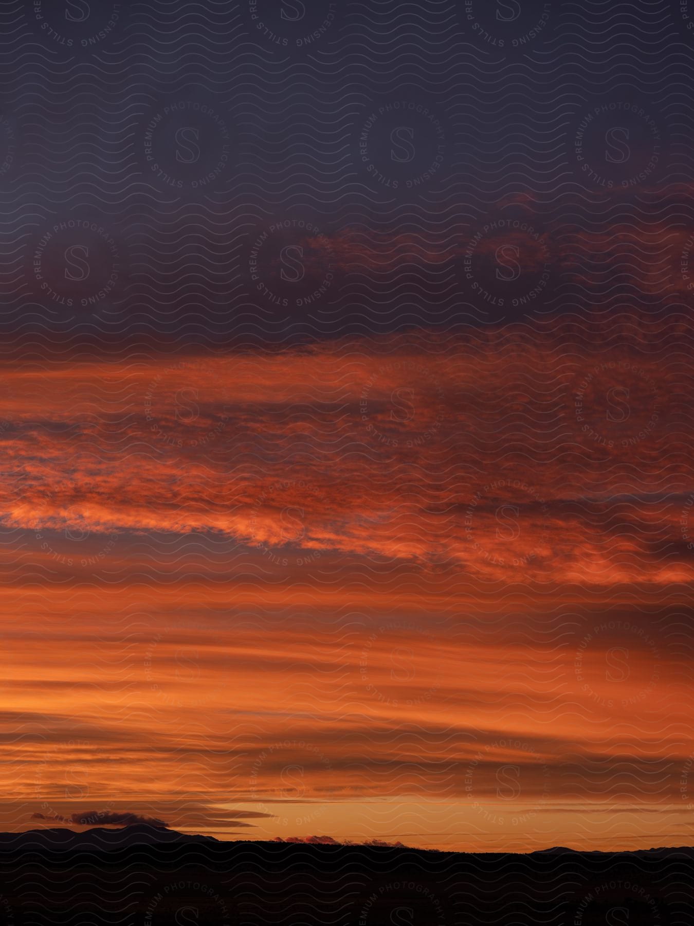 Deep red clouds hang over a silhouette of mountains and land at sunset in new mexicos white sands national park