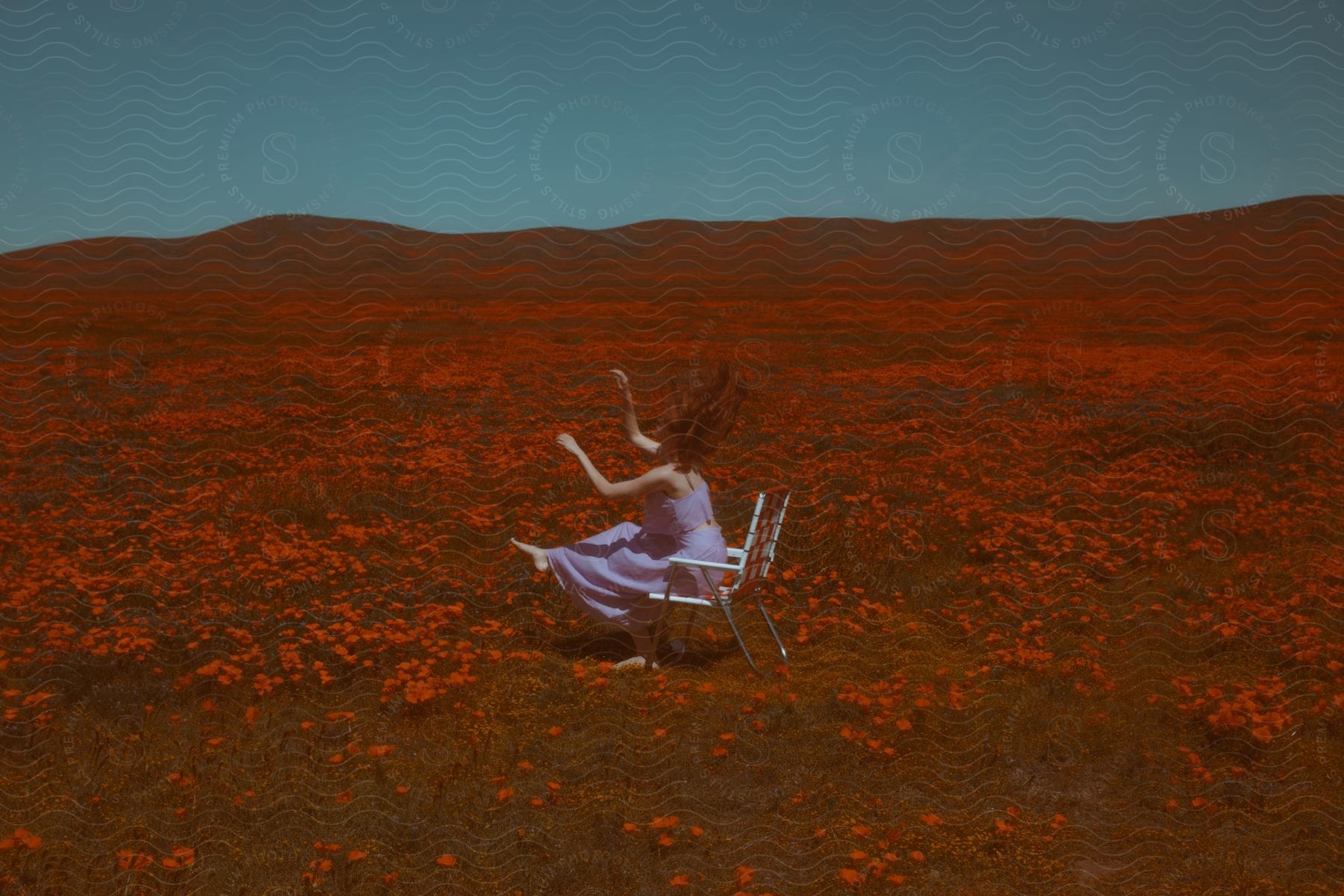 A woman sitting in a chair in a field of orange flowers with her arms up