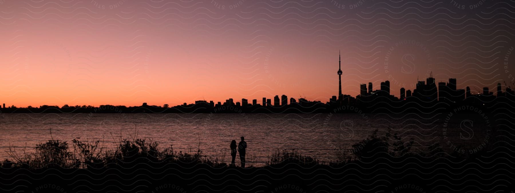 Coastal landscape with two silhouettes and buildings in the background on the horizon