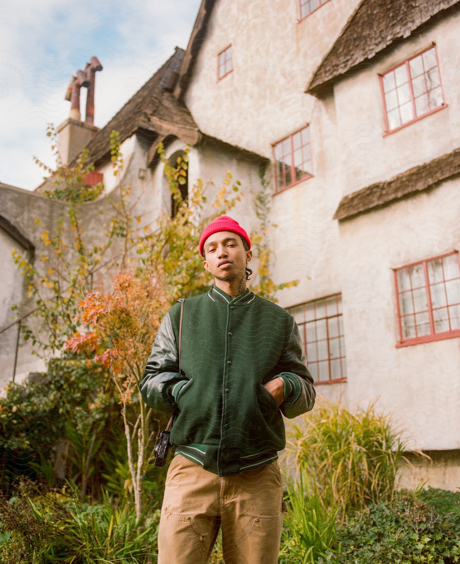 A man poses in front of a big house next to plants