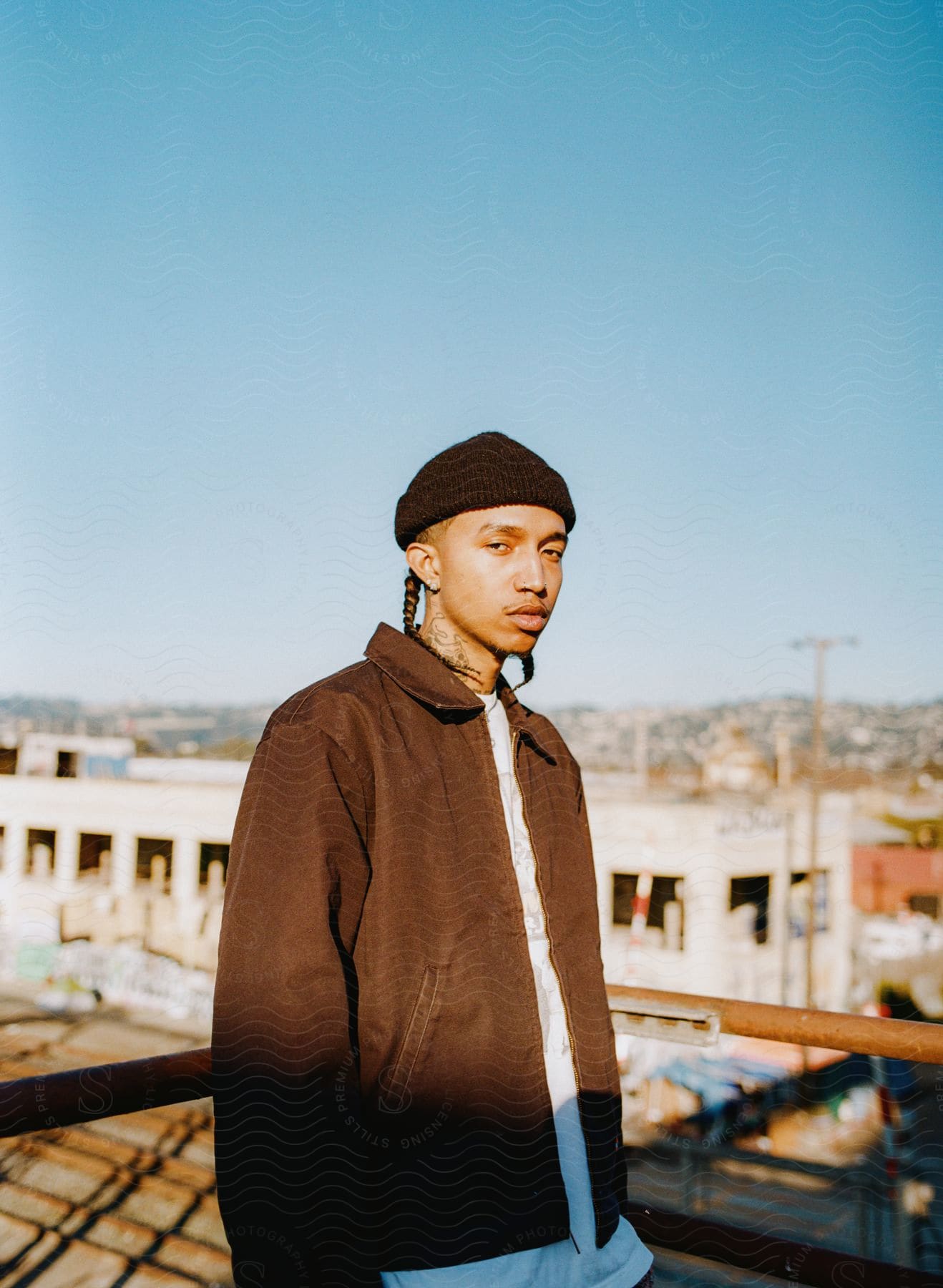 A young man in a beanie and jacket poses by a railing