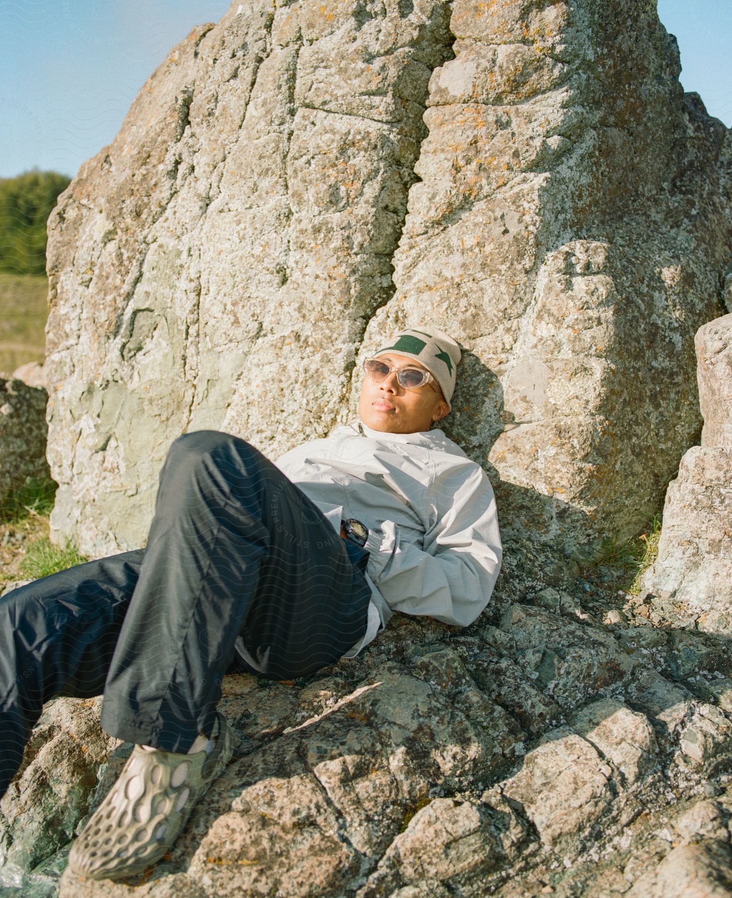 A happy person wearing sunglasses sitting on a rock in nature