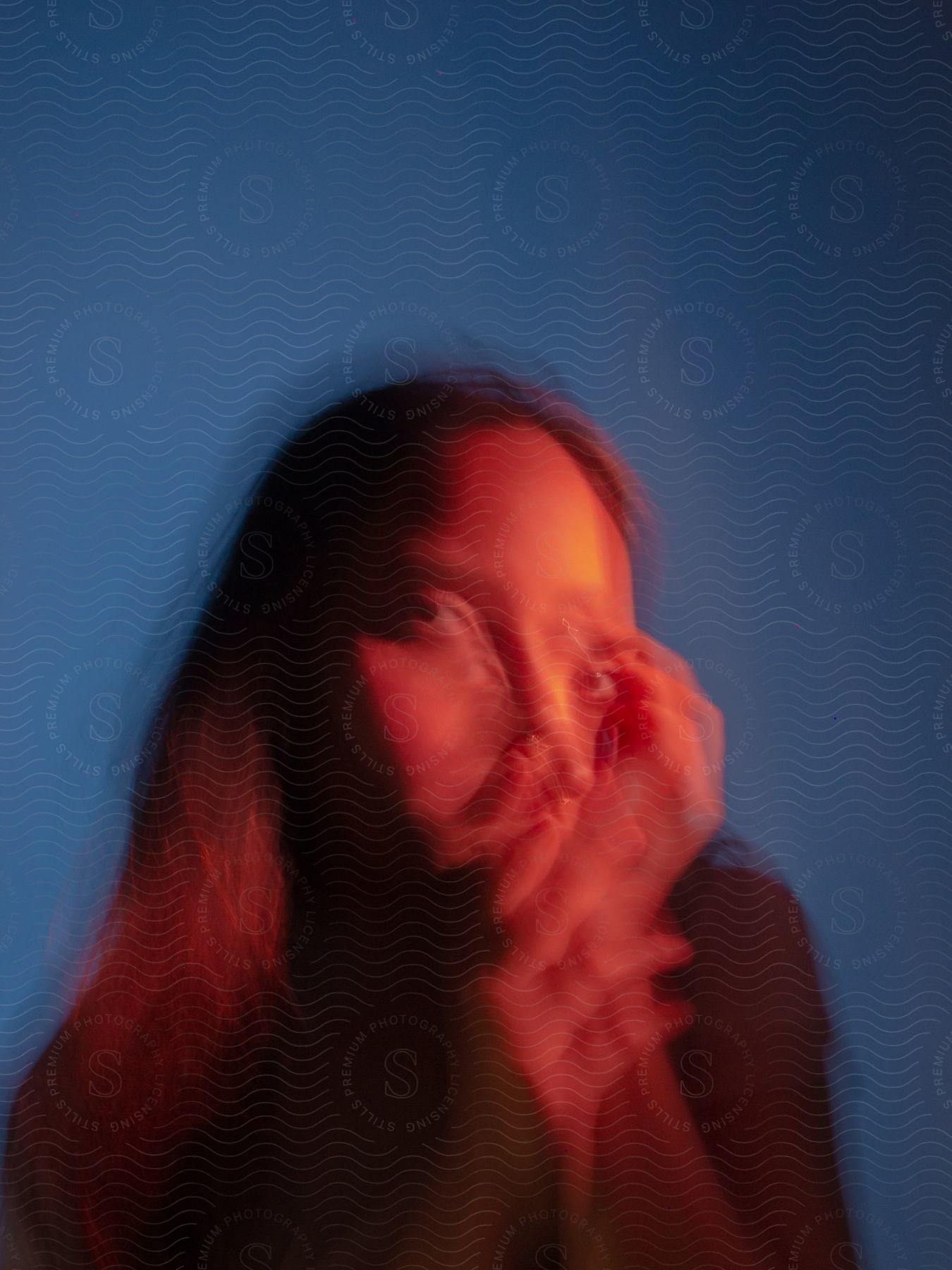 A blurry profile of a woman with her hand on her face looking forward