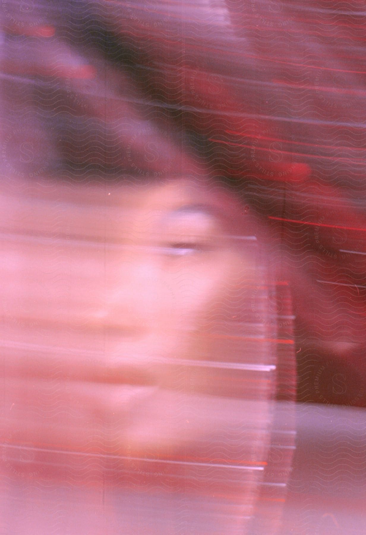 Blurred closeup of a young womans face leaving color trails under red lights