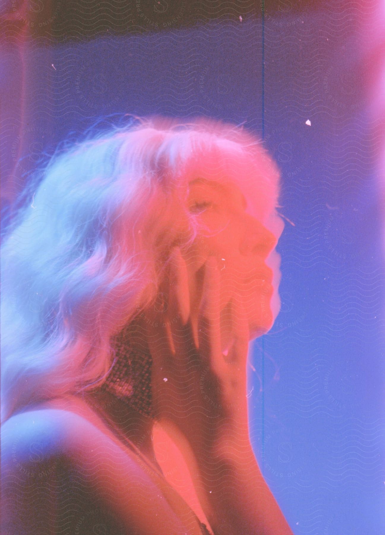 Blurred close up of a young womans face with wavy white hair under red lights
