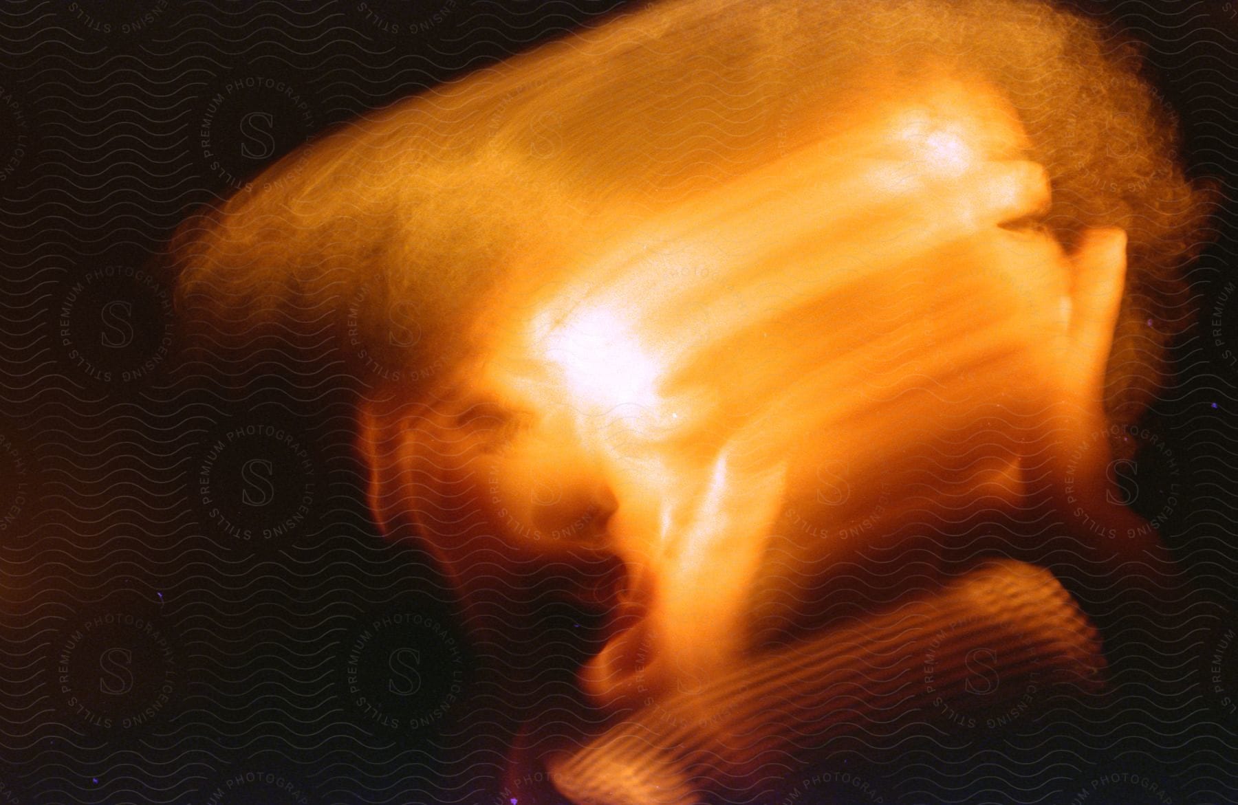 A womans face is distorted by motion blur under amber lights in a double exposure photograph