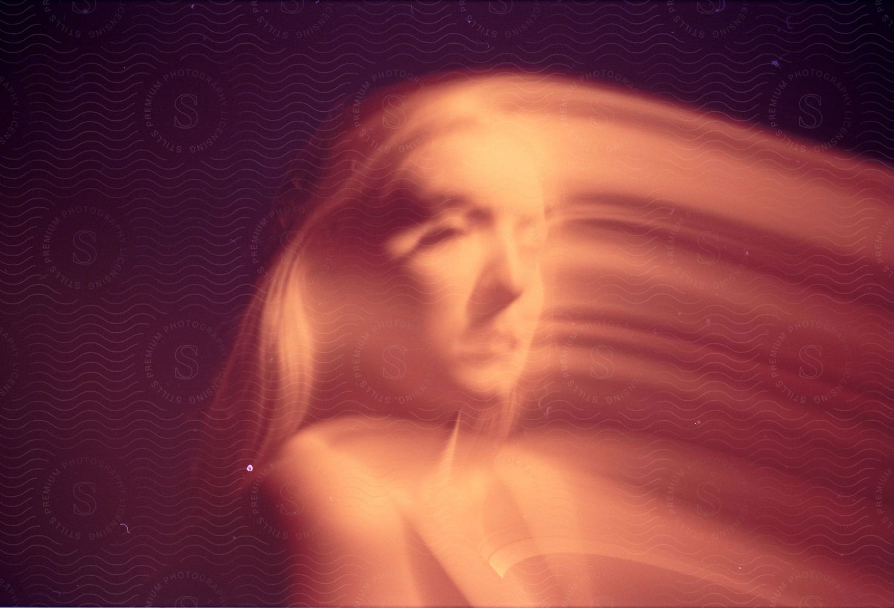 A female face is distorted by red and golden lights in a double exposure with motion blur