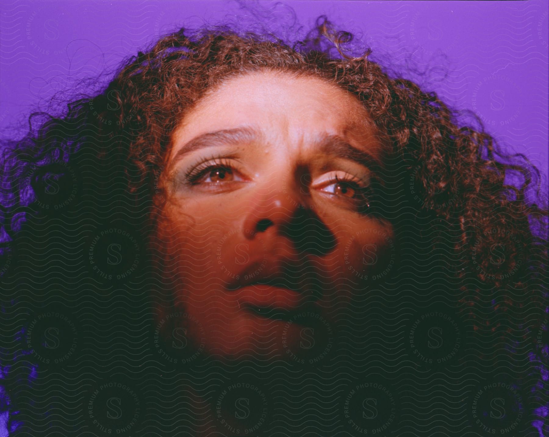 Stock photo of close up of a young woman with curly hair against a violet background