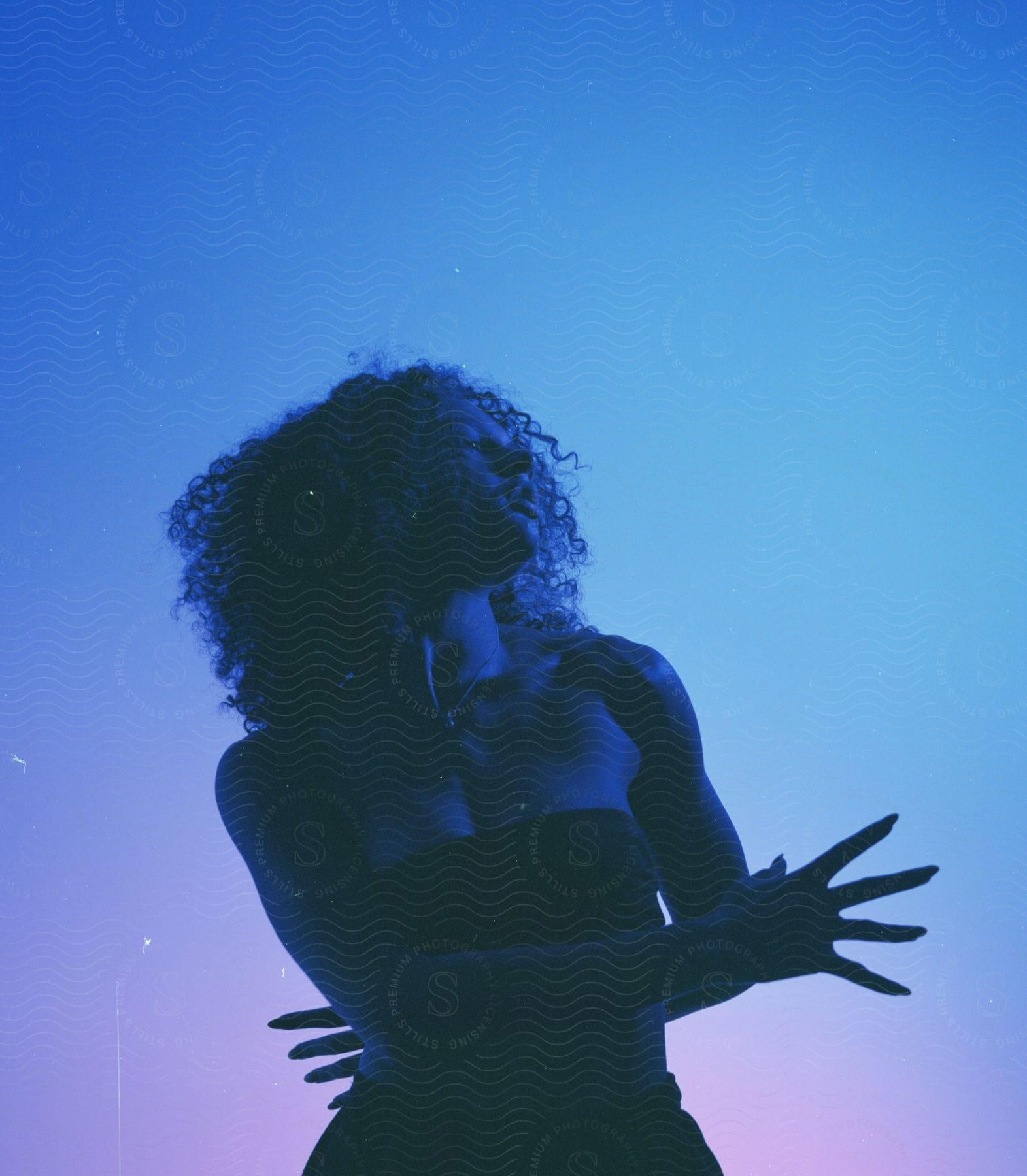 A woman poses in a bandeau top and skirt against a blue and pink background.