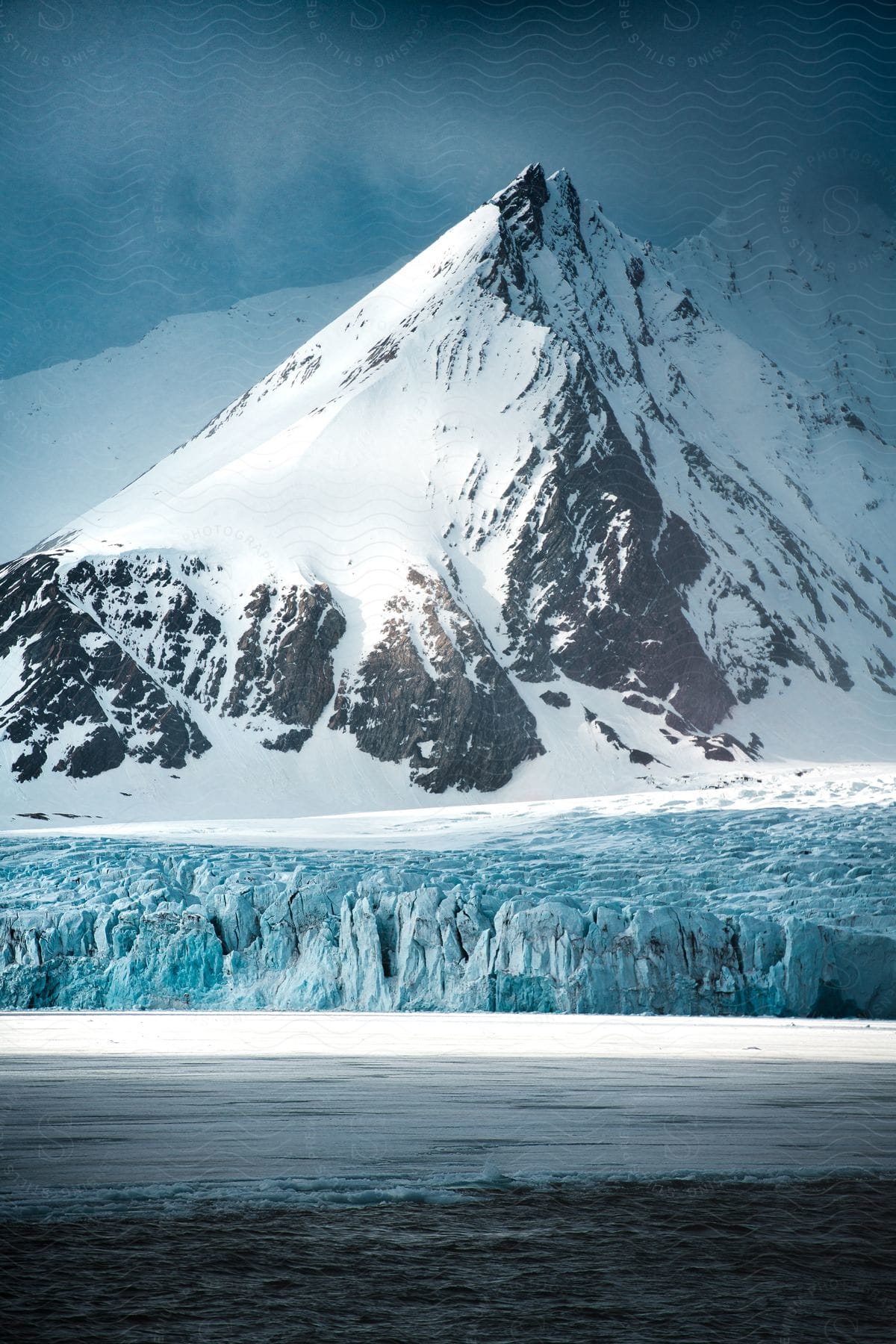 Calm water flows next to icy bank with snowcovered mountain in background