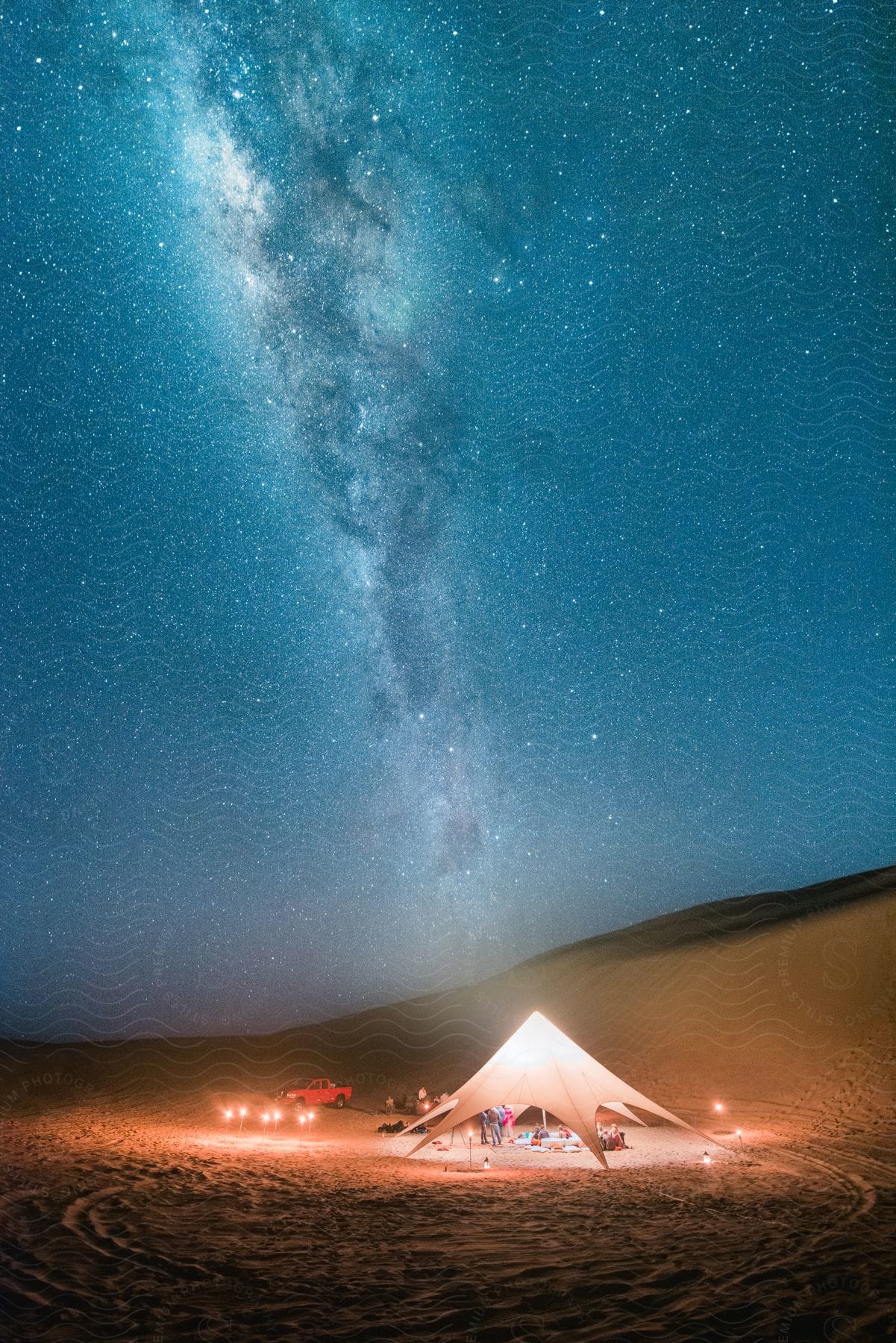 A Small Group Of People Stand Under A Tent In The Desert With A Galaxy In The Night Sky