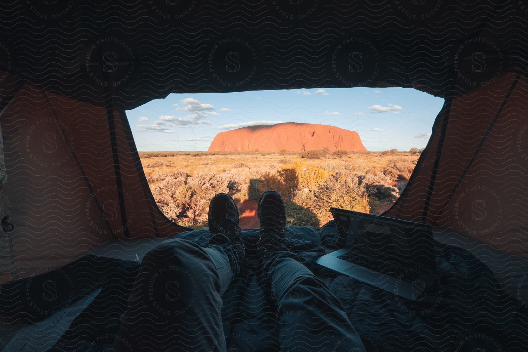 A person lies next to a laptop inside a tent with a large mesa visible through the door