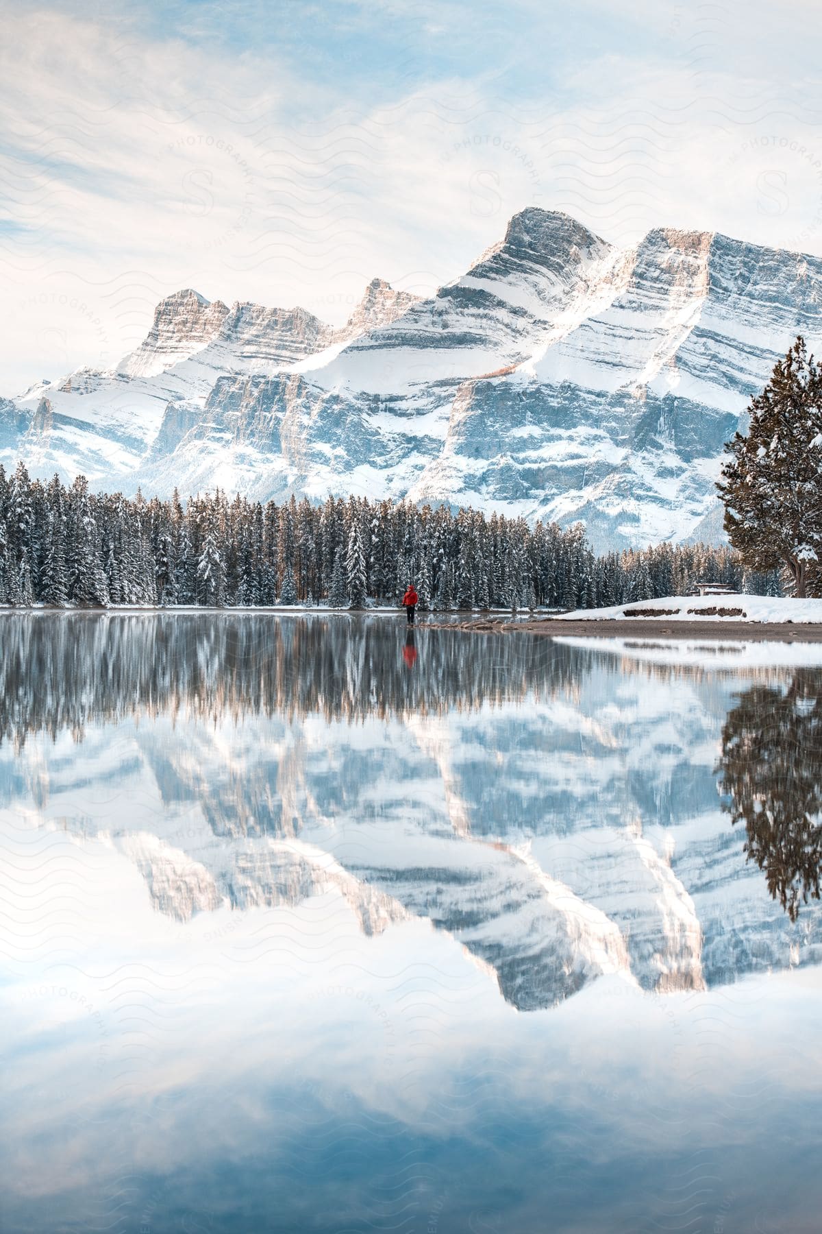 A person wearing a red coat and black pants stands by two jack lake in canada