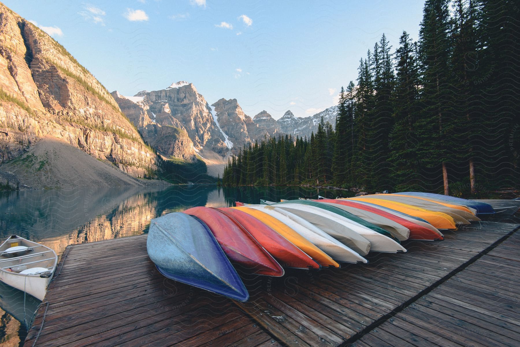 Colorful canoes lined up on a pier with mountains in the background situated on a lake