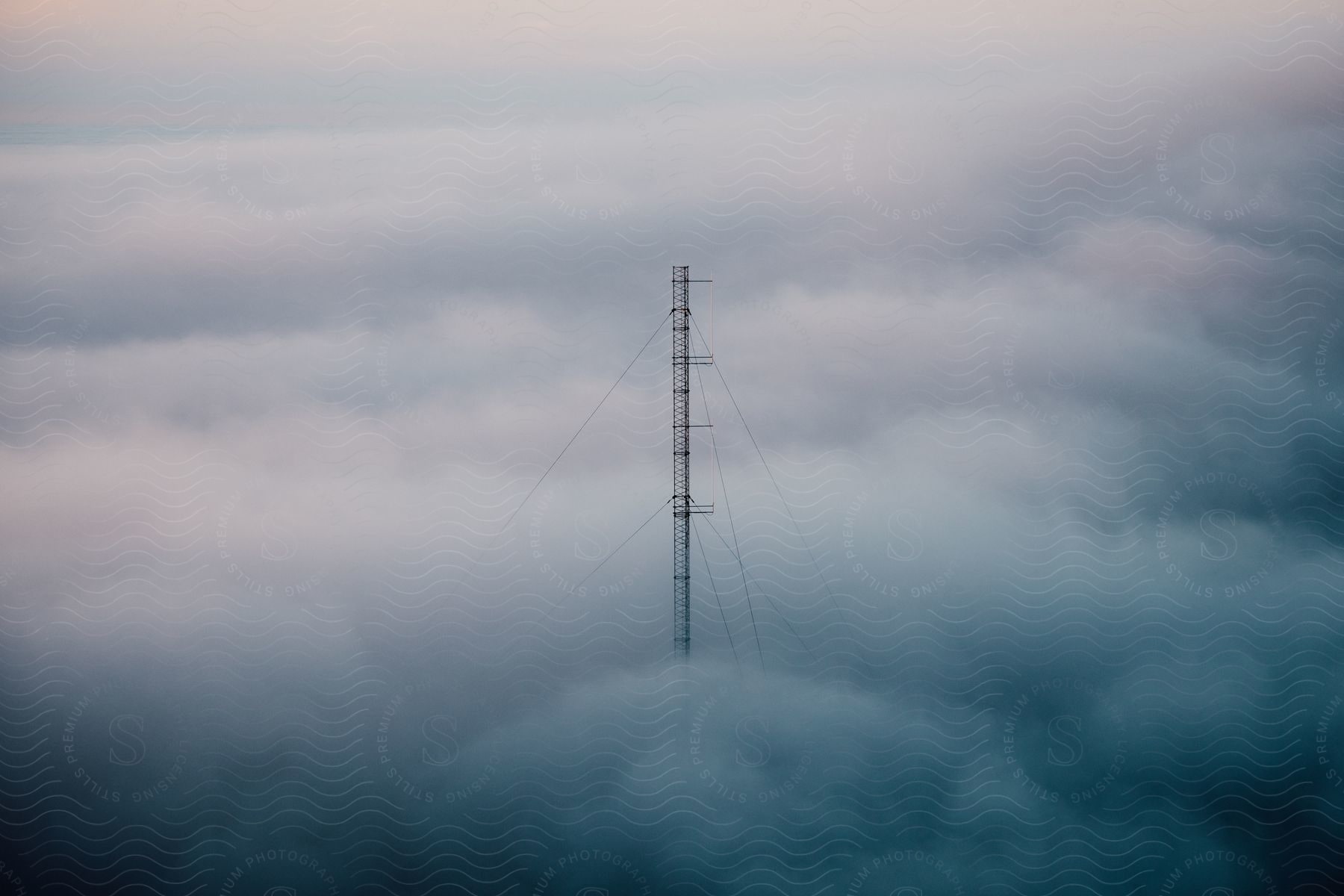 A tower with bracing cables stands high above the clouds