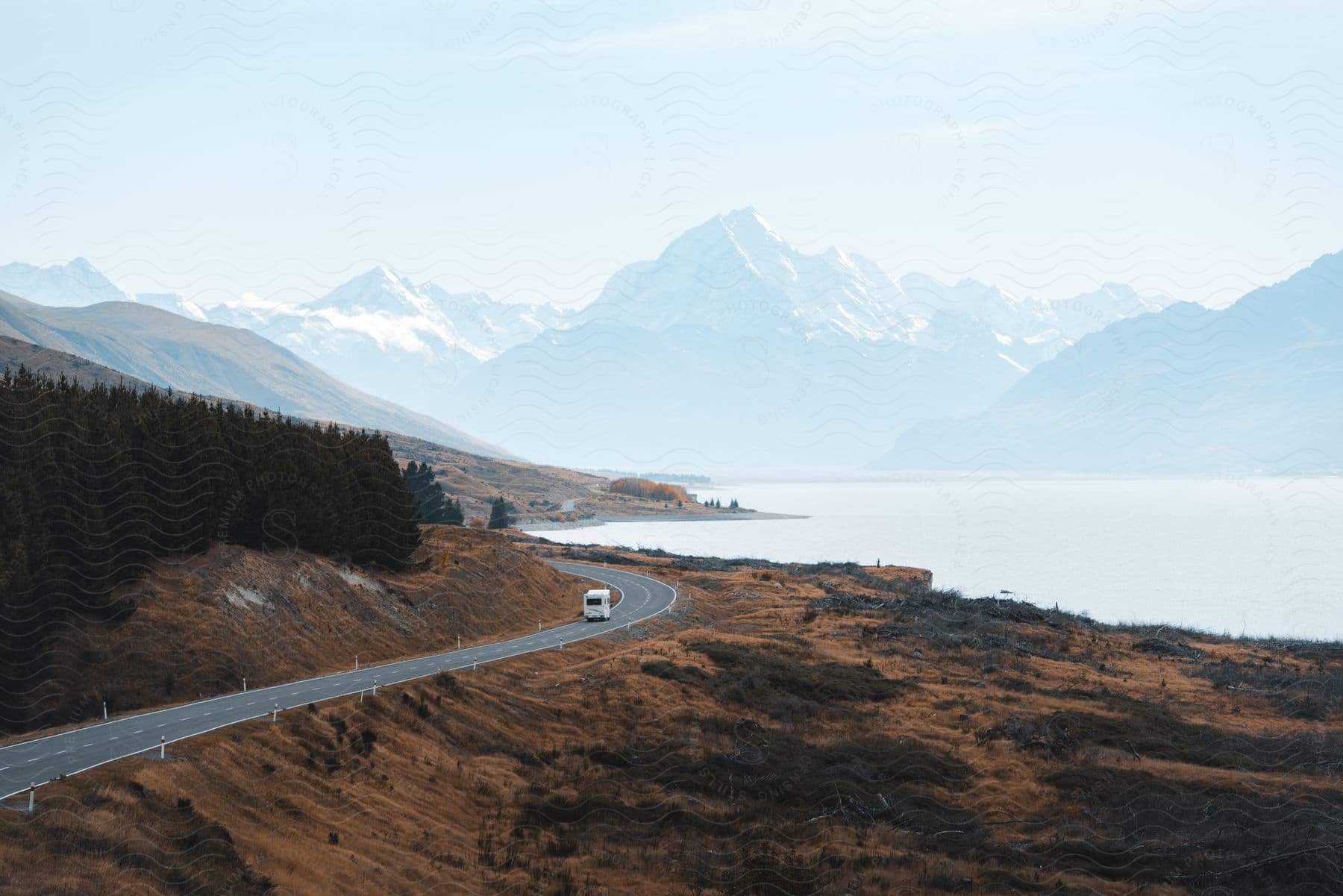 A camper drives down a rural highway below a mountain range in new zealand