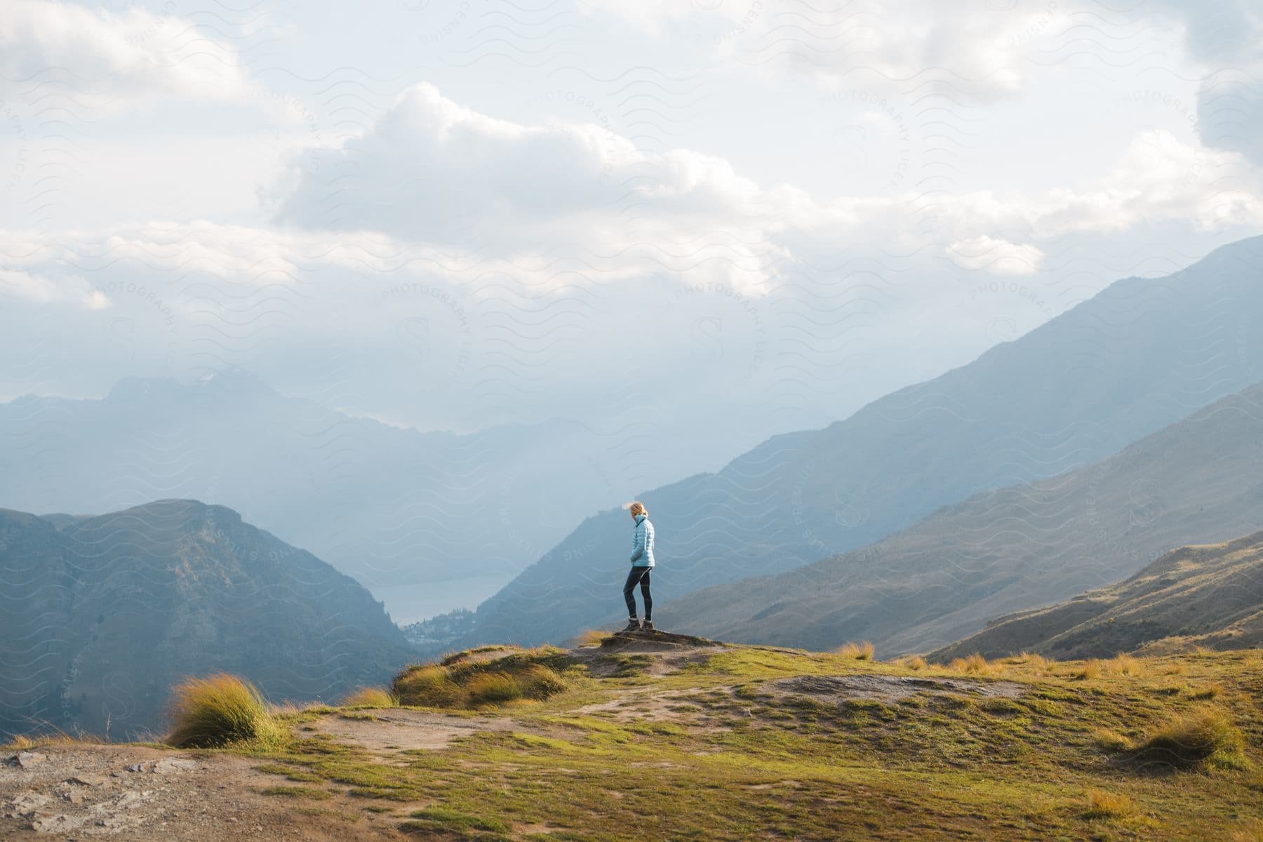 Stock photo of a woman looks downhill at a valley with clouds above mountain tops