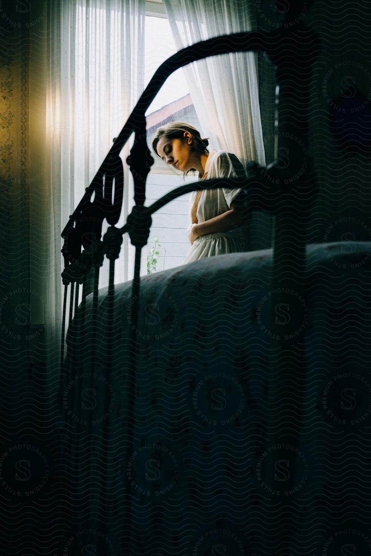 Stock photo of a woman holds herself against her window in a dark room on a bright day