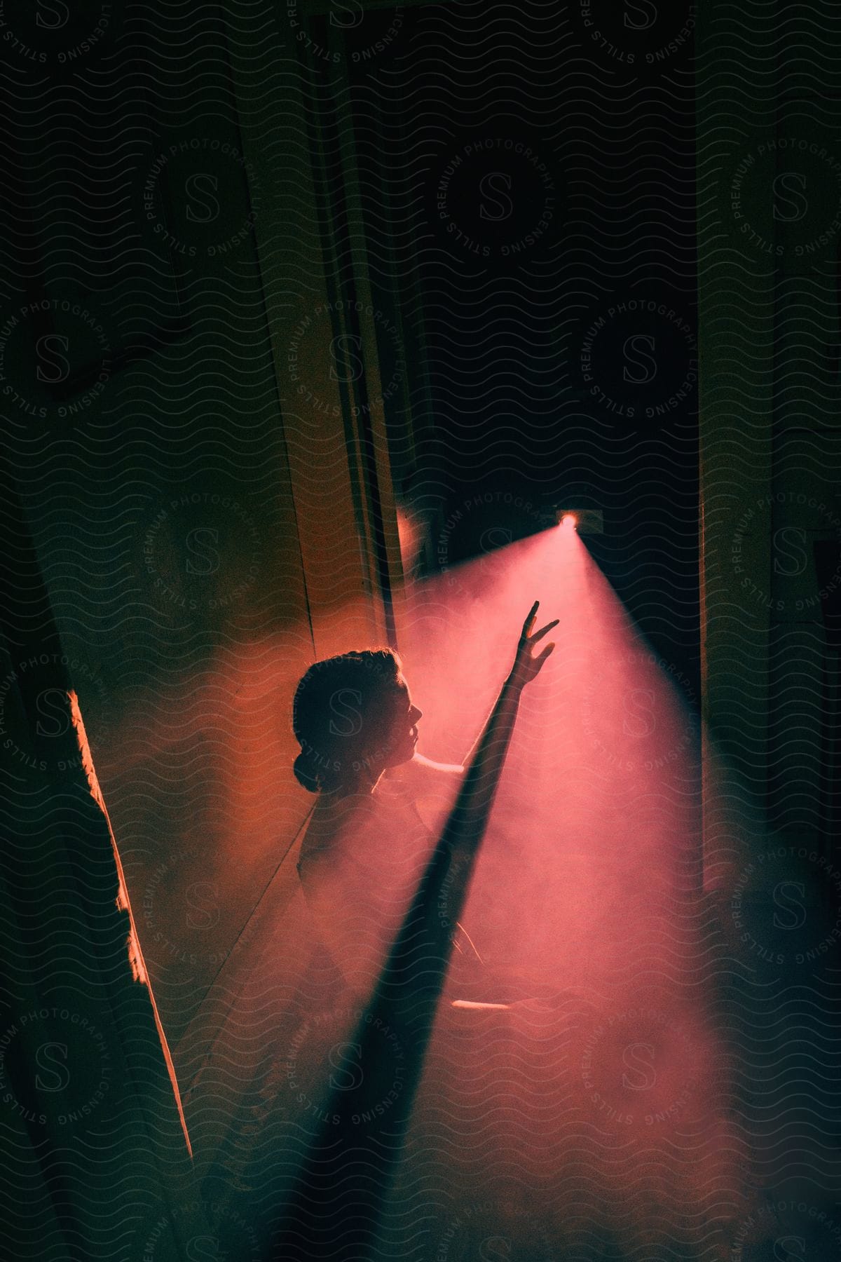 A determined woman stands in a dimly lit room illuminated by a ray of light from a partially opened door