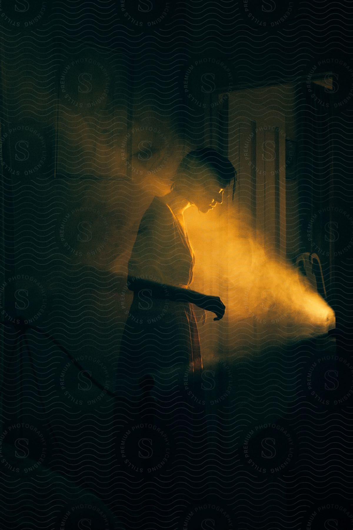 A woman standing in a dark room in front of smoke as she looks downward