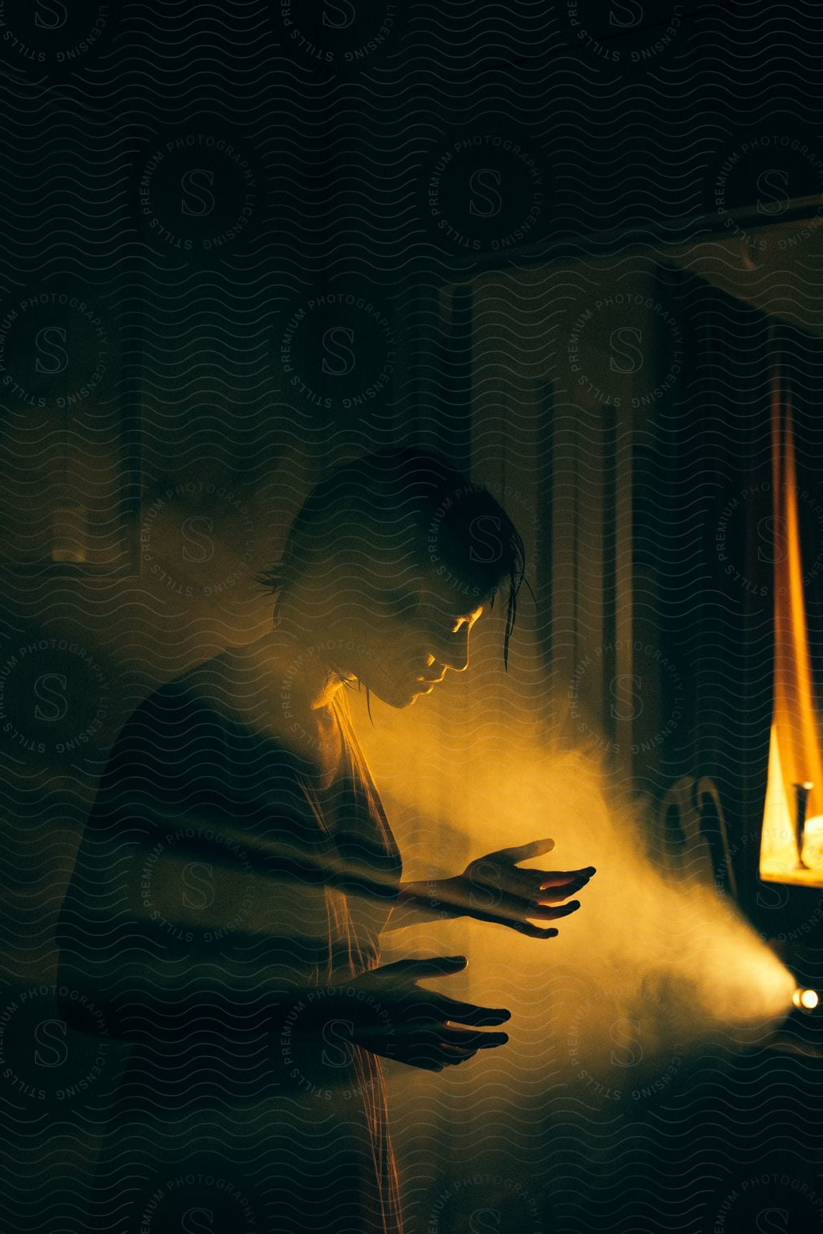 A silhouette of a woman standing with her hands in front of her with steam rolling over her face indoors