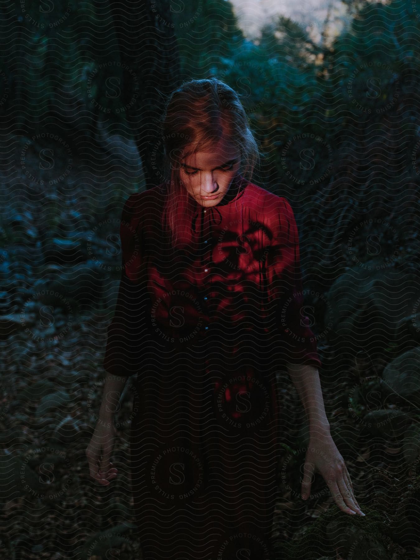 Young woman in red dress walking through a forest with shadows cast across her chest