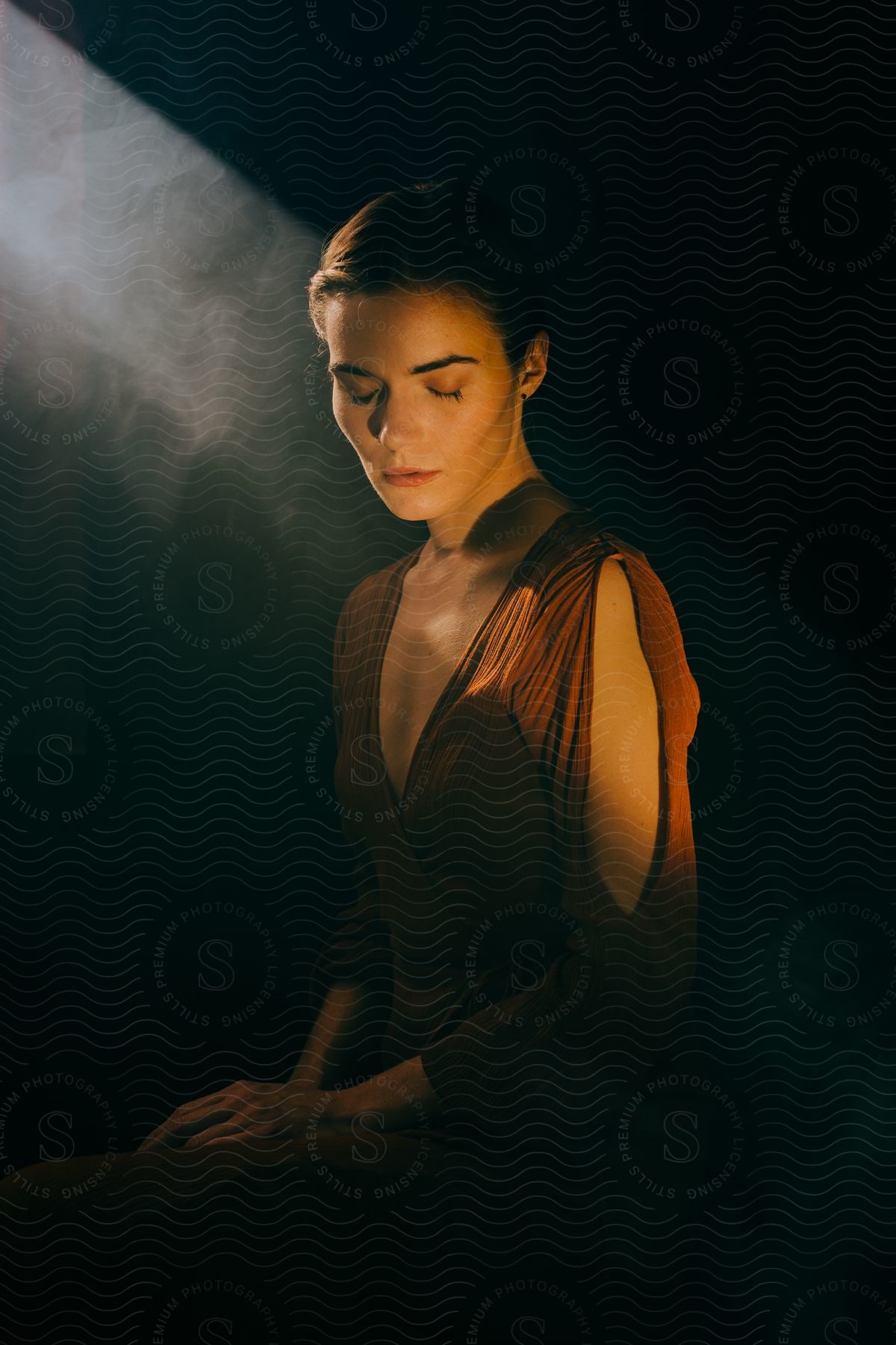 A woman looking down in a dimly lit room with smoke around her