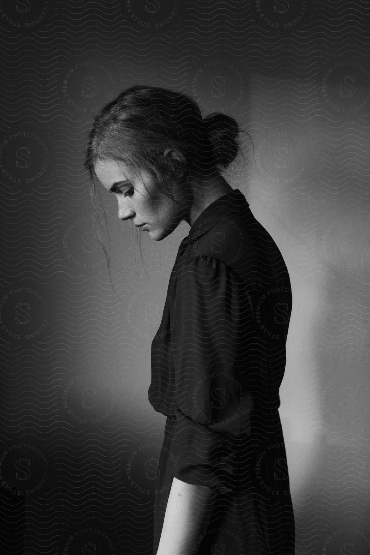 A woman dressed in black stands with her hair in a bun captured in black and white