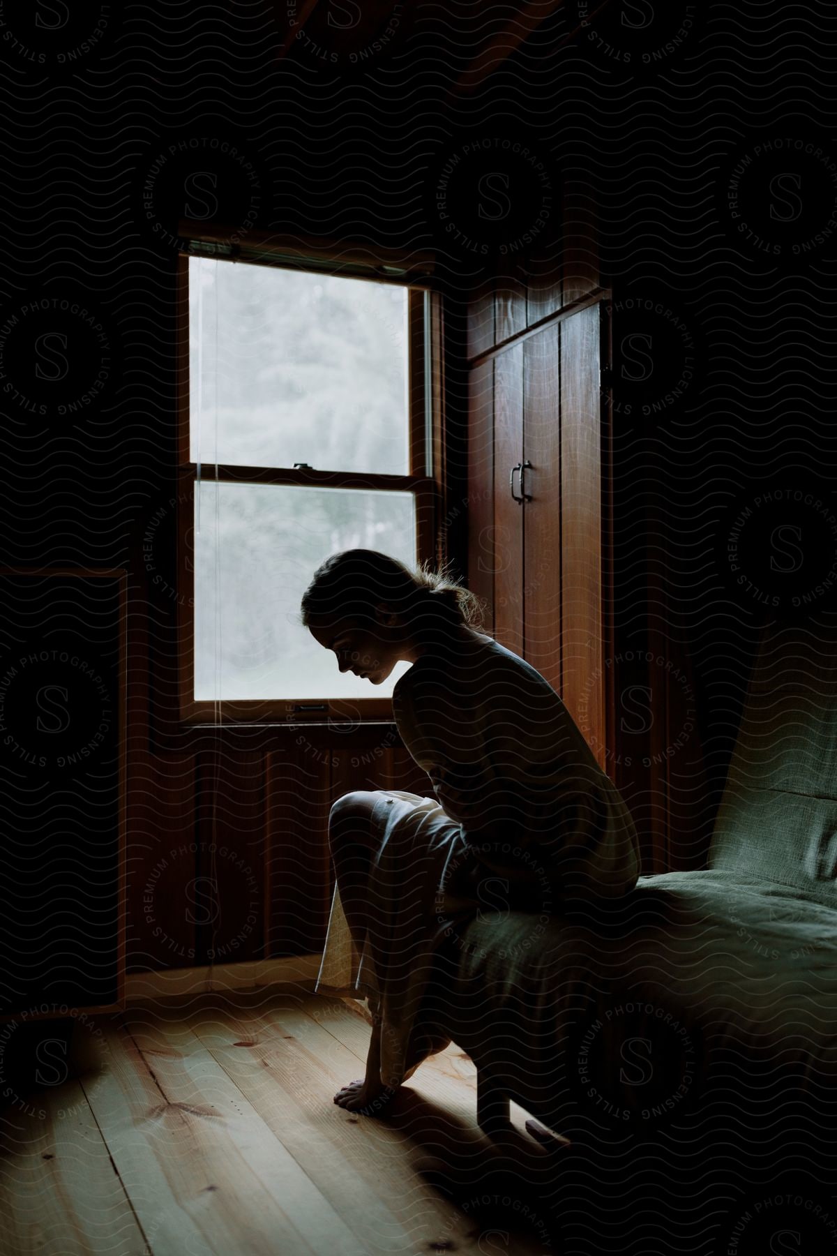 A woman sitting on the edge of a sofa next to a window indoors