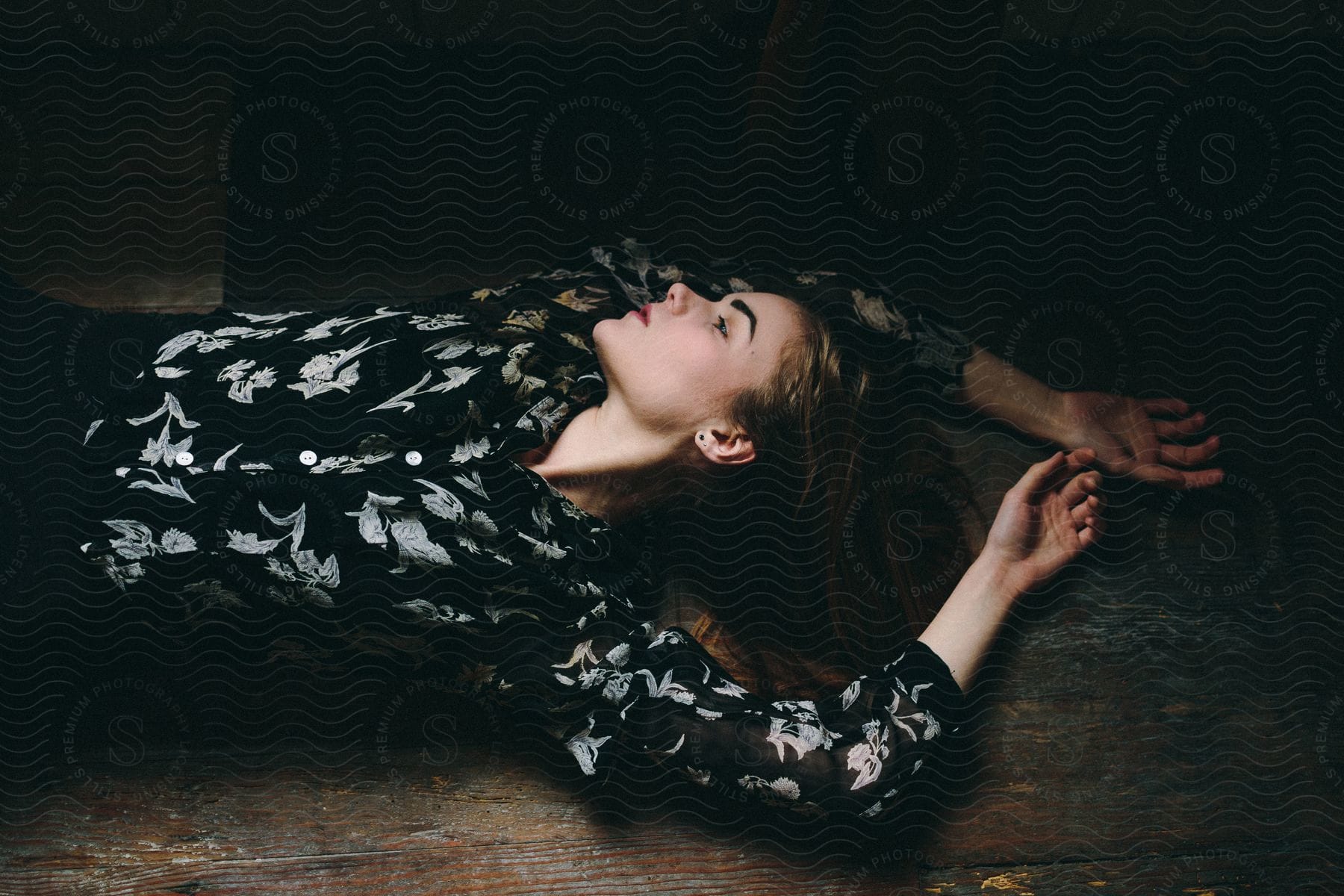 A woman laying down on a wooden floor with her eyes closed and arms raised above her head