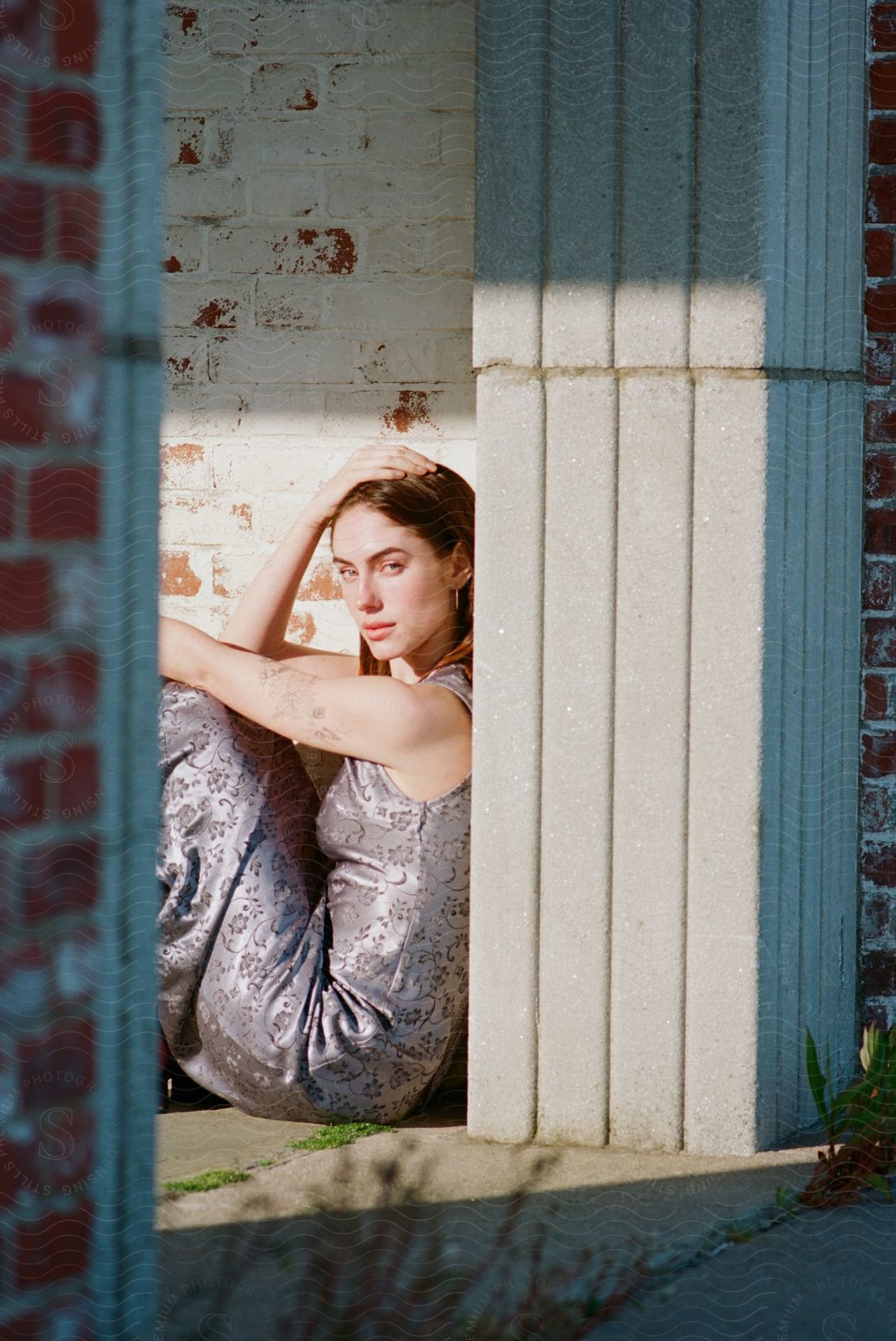 A young woman models and poses for pictures sitting on the floor and leaning against the wall as the sun brightens her