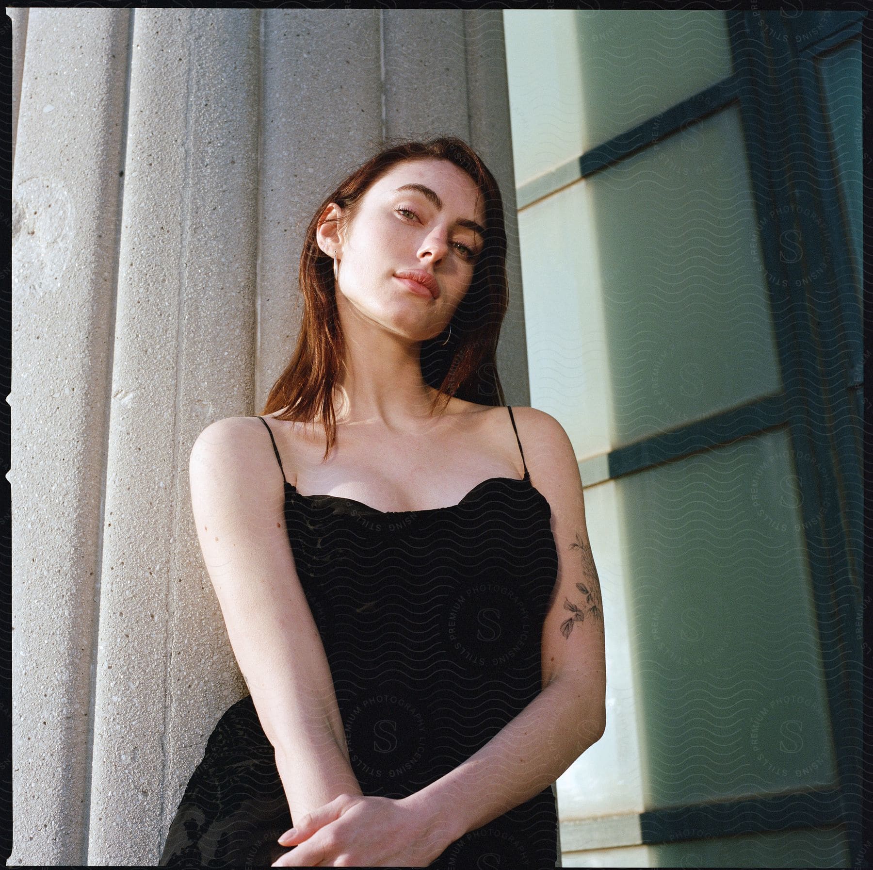 A woman wearing a black spaghetti strap dress stands next to a building