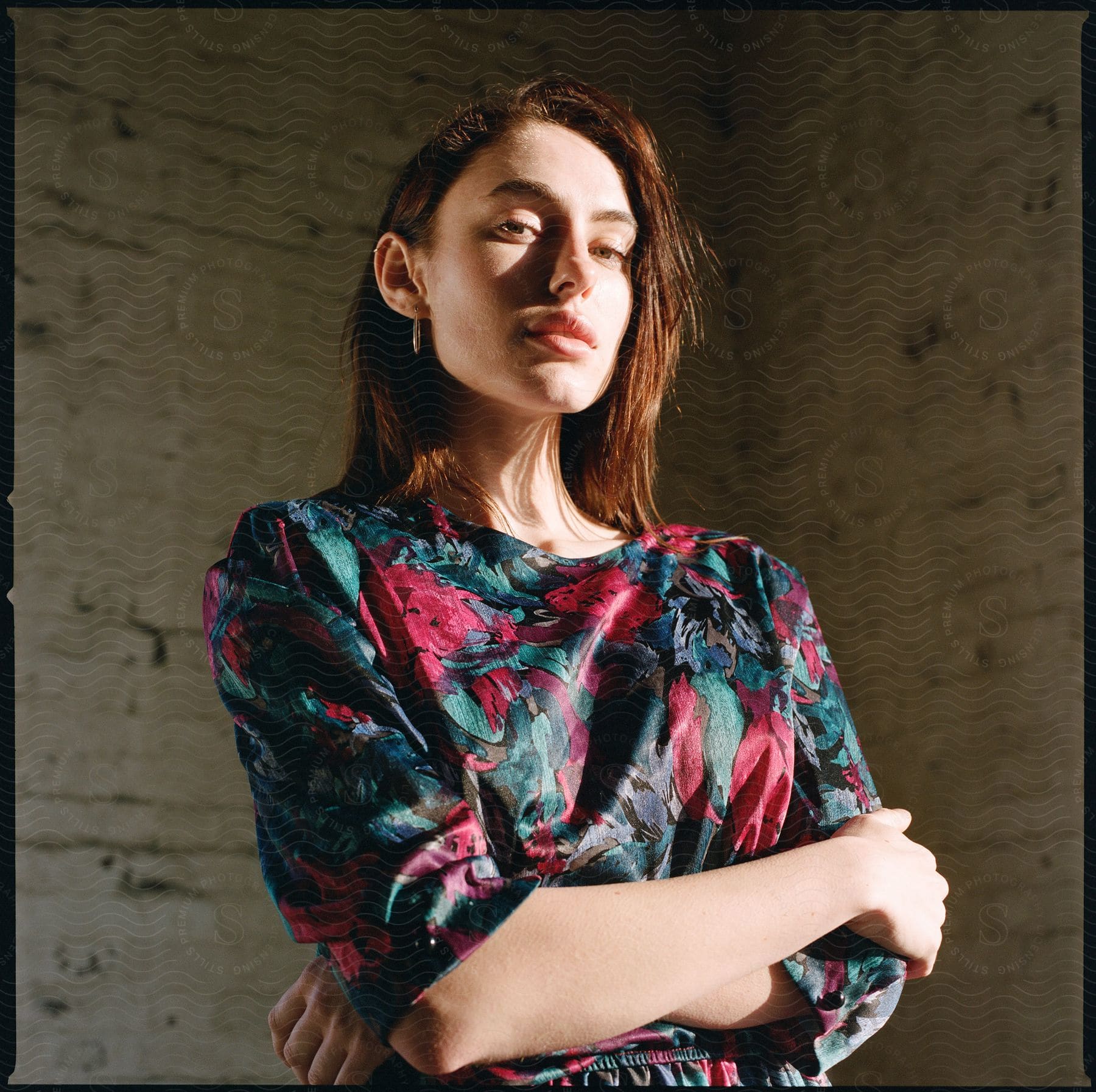 A young woman with crossed arms dressed in a colorful blouse posing for a picture