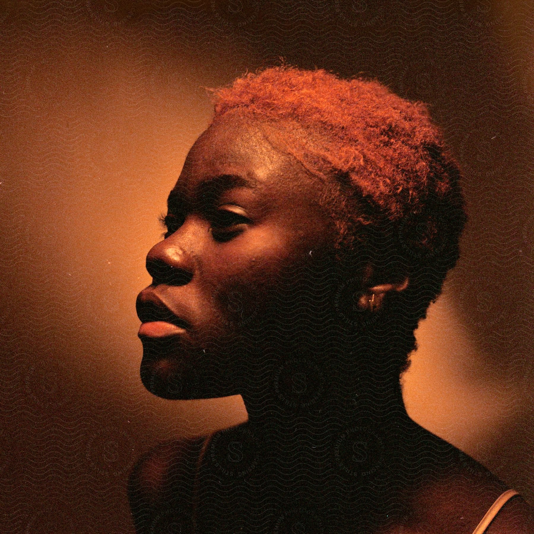 A young black woman with short, light red hair poses against a brown background.