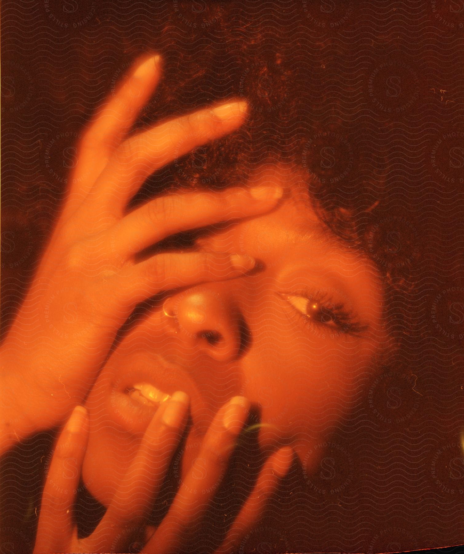 Black woman with hand covering one eye in softly lit room