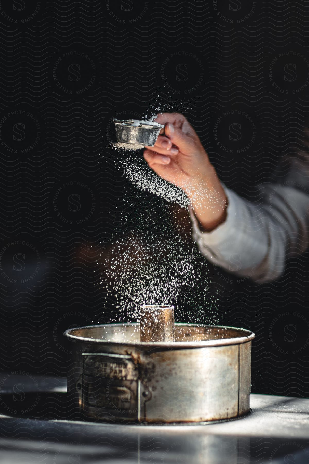 Stock photo of hand adding icing sugar to a cake in a mold in a kitchen