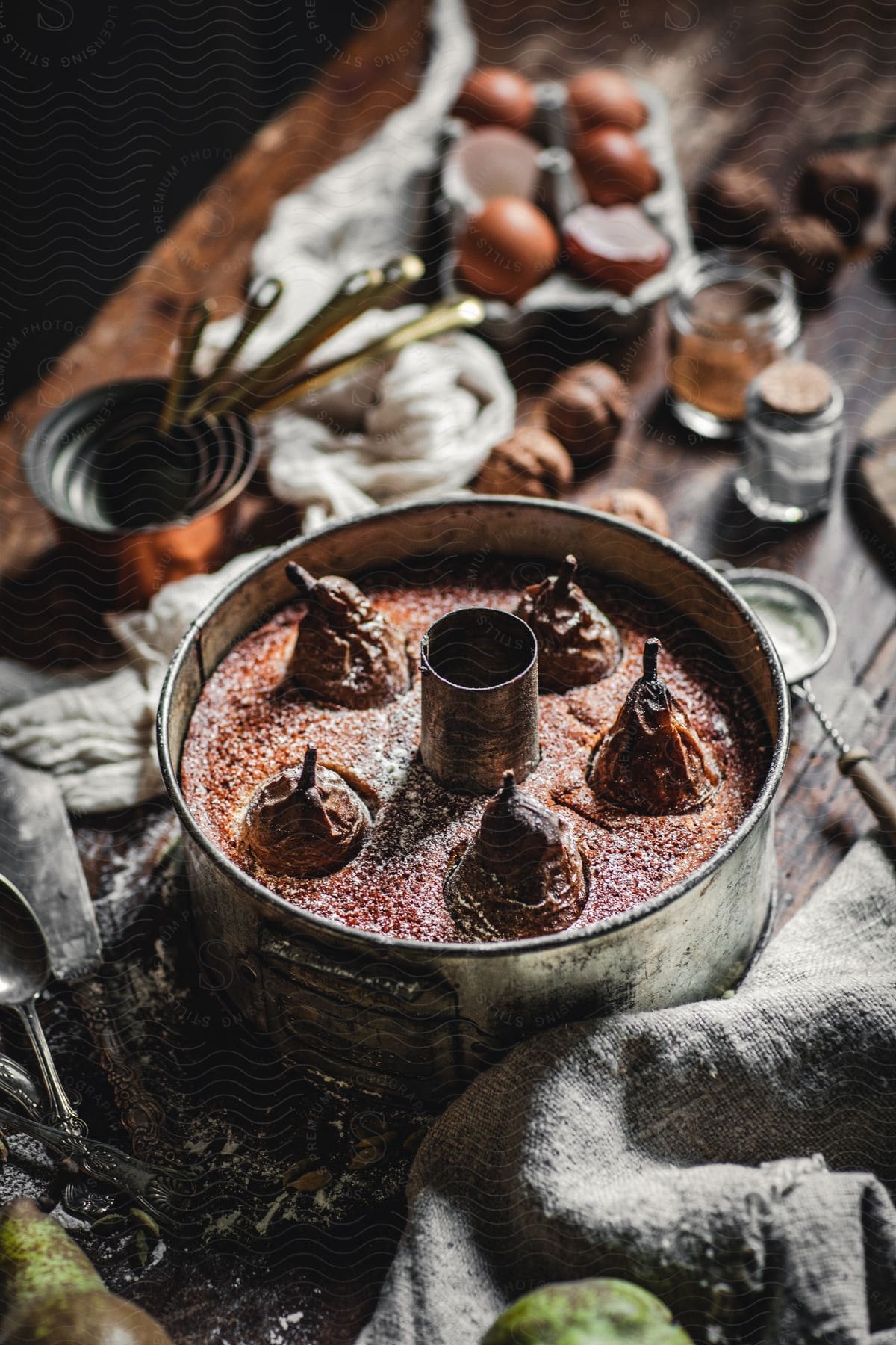 Bundt cake with pears measuring cups eggs and mixing spoons on a wooden table