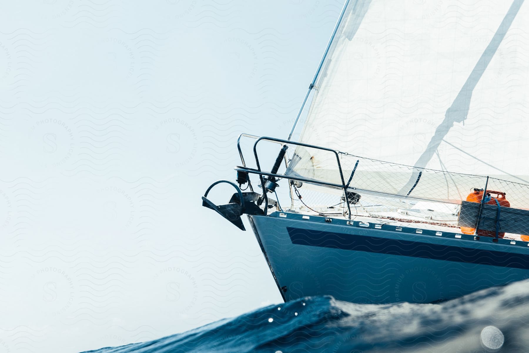 A sailboat is illuminated by the sun as it navigates rough water waves